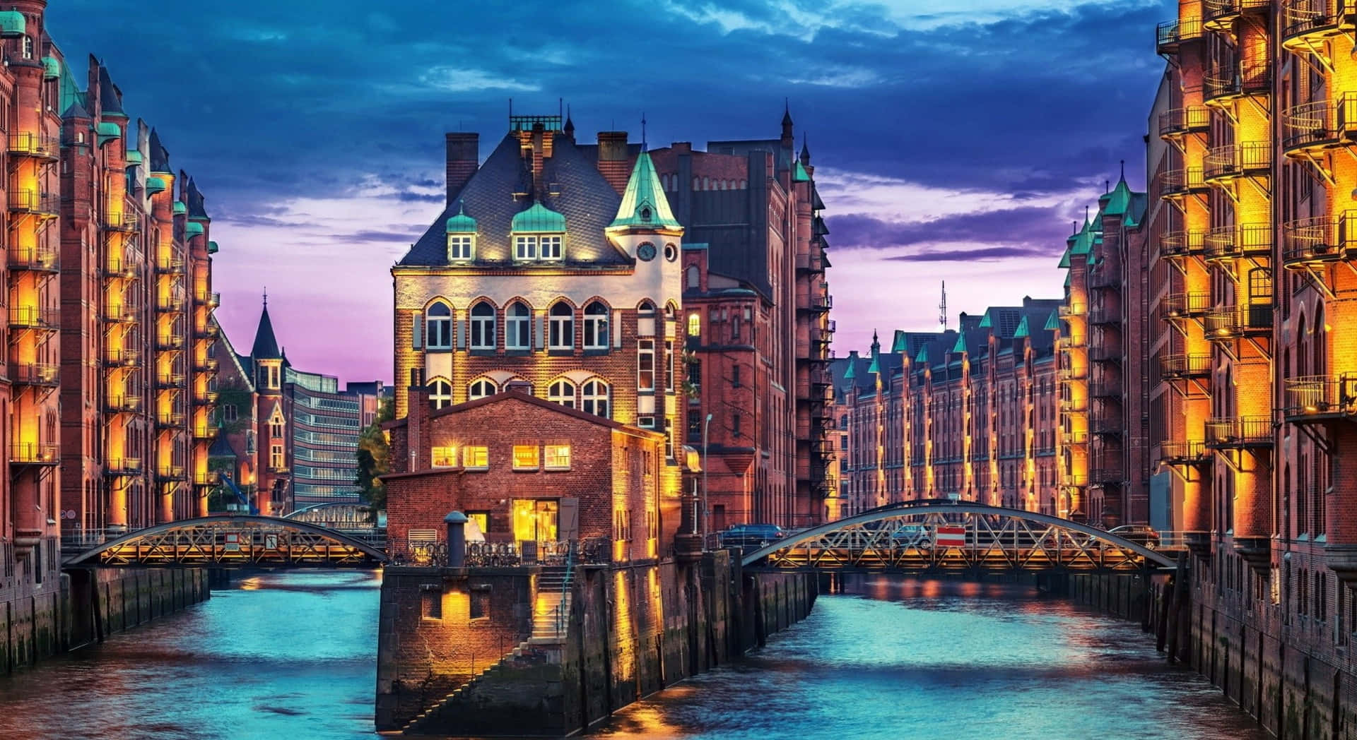 Europe 桌布 壁紙 — 充滿活力的暮色運河場景，歷史悠久的磚造倉庫在紫色和藍色的天空下溫暖地發光。