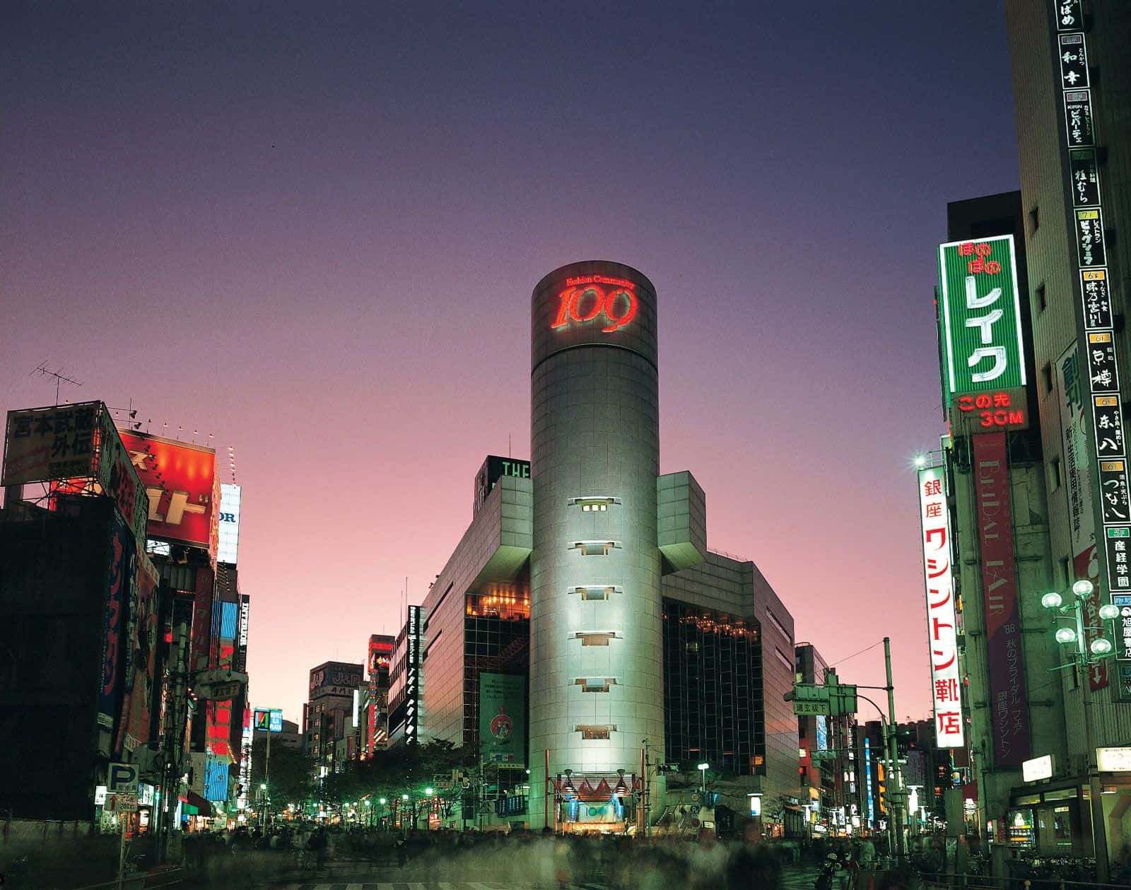 東京 桌布 壁紙 — 充滿活力的東京城市景觀，黃昏時分，霓虹燈閃爍，一座高聳的圓柱形建築在紫色天空下顯示「109」。