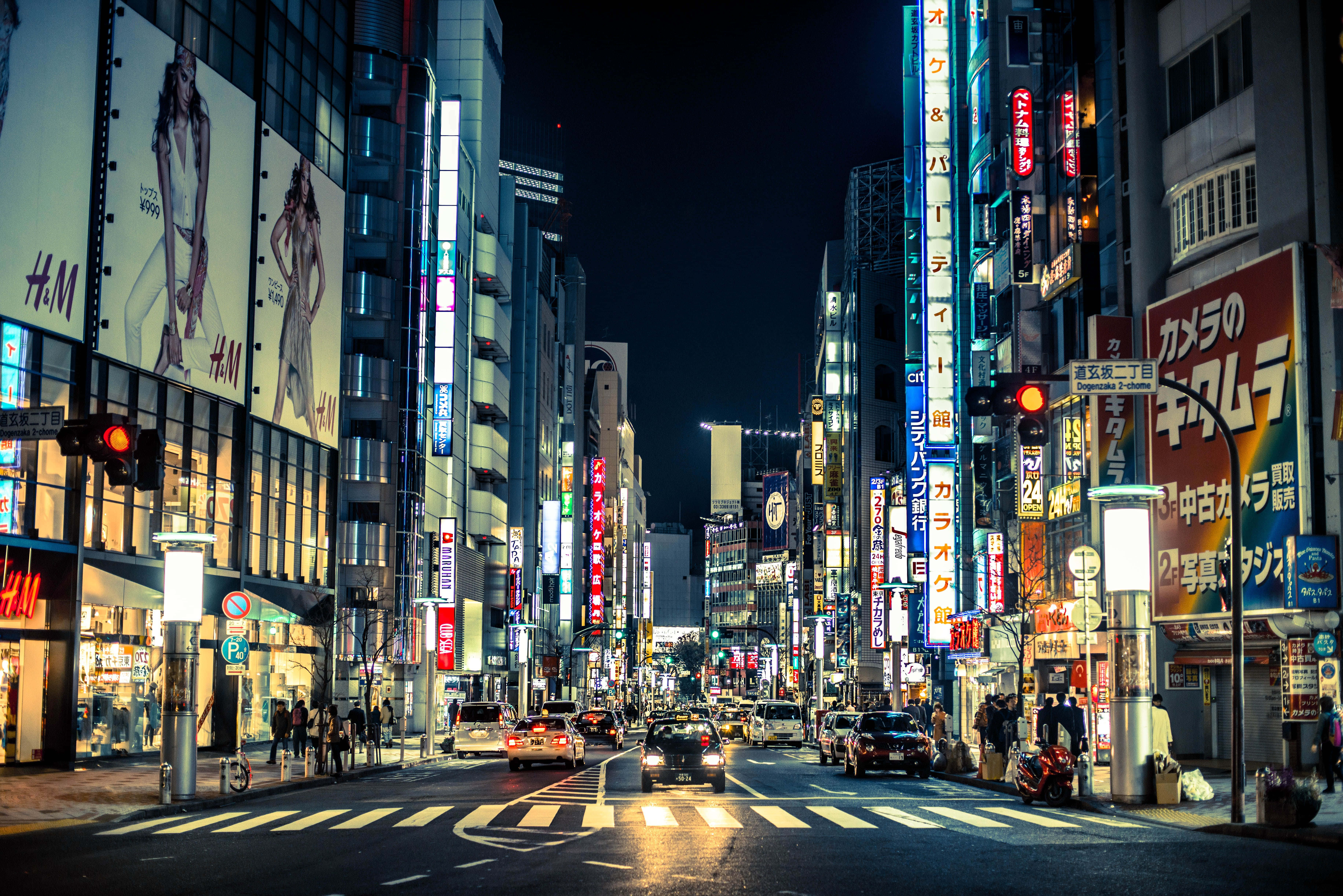Cartoon City 桌布 壁紙 — 充滿活力的東京夜晚街道，霓虹燈閃爍，發光的招牌、汽車和熙攘的行人穿梭在高聳建築物之間。