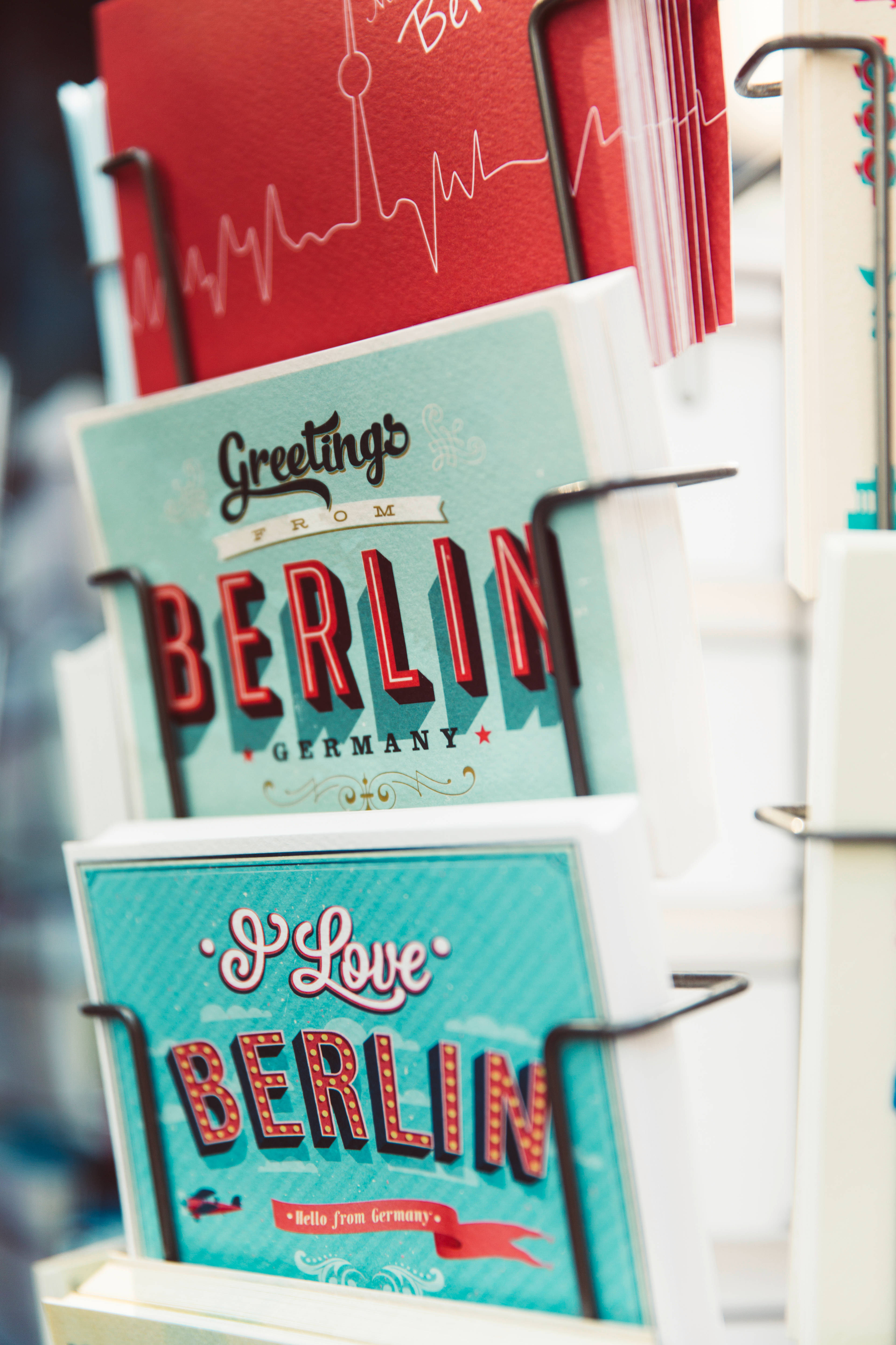 Berlin 桌布 壁紙 — 充滿活力的柏林復古明信片（紅色和藍綠色）展示在帶有心跳線設計的金屬架上。