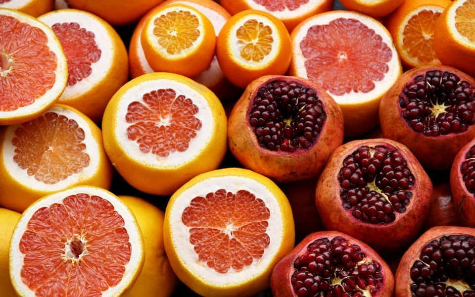 Winter Fruits 桌布 壁紙 — 充滿活力的柑橘類水果（包括葡萄柚和石榴）切半特寫，展現多汁的果肉和種子。