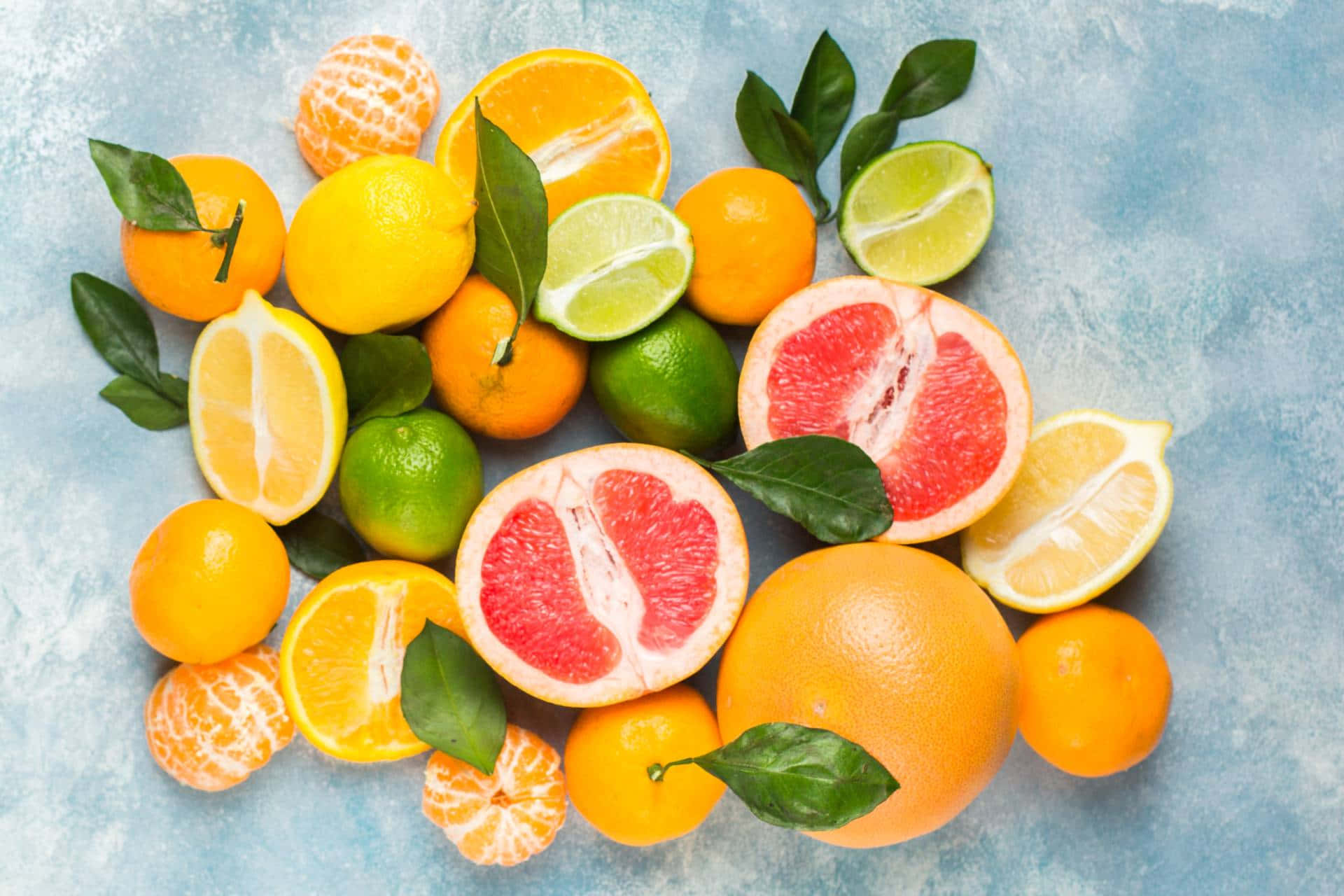 Fruit 桌布 壁紙 — 充滿活力的柑橘類水果，包括西柚、檸檬、青檸和柳橙，搭配葉子排列在帶有紋理的藍色表面上。