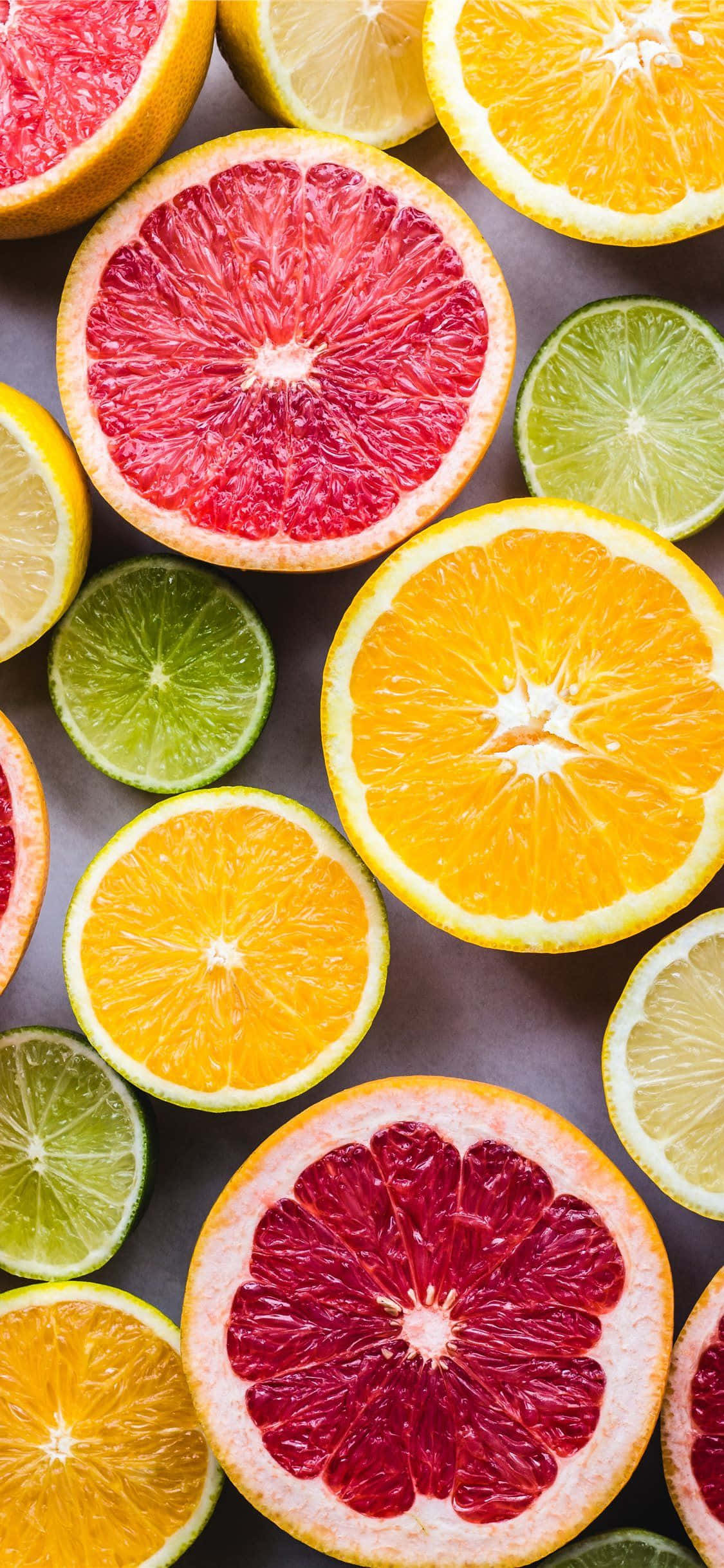 food iPhone 桌布 壁紙 — 充滿活力的柑橘類水果橫切面，如葡萄柚、柳橙和萊姆，以色彩繽紛的平鋪構圖排列。