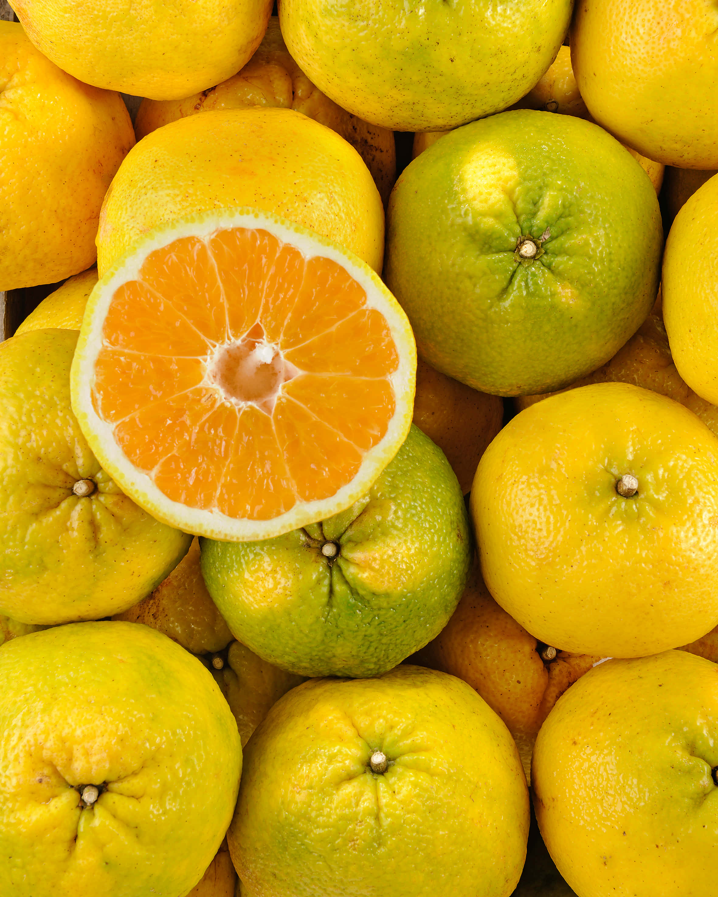 Fruits 桌布 壁紙 — 充滿活力的柑橘類水果特寫，其中一個切半的柳橙露出多汁的果瓣，周圍環繞著完整的黃色和綠色柳橙。
