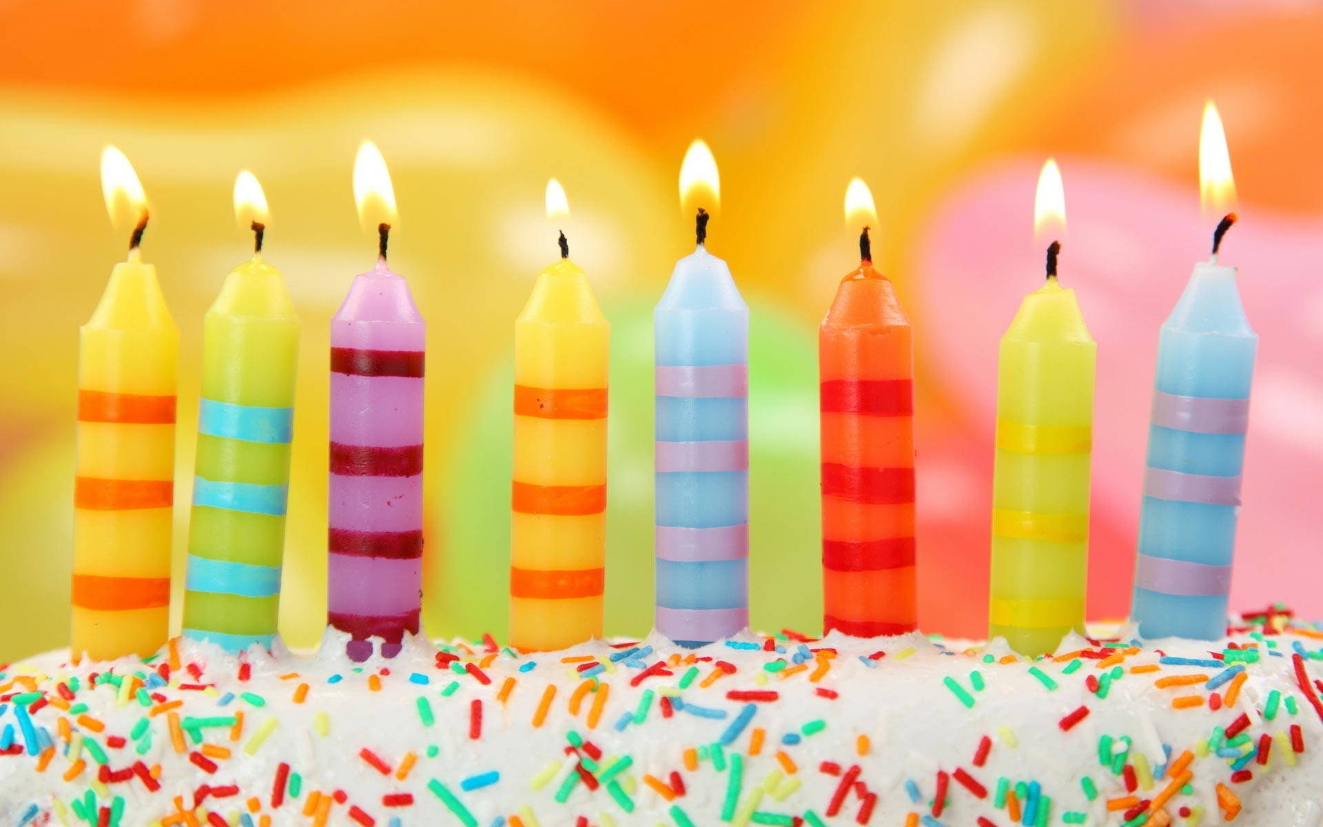Cake 桌布 壁紙 — 充滿活力的條紋生日蠟燭在灑滿彩色糖粒的蛋糕上閃爍，背景溫暖而模糊。
