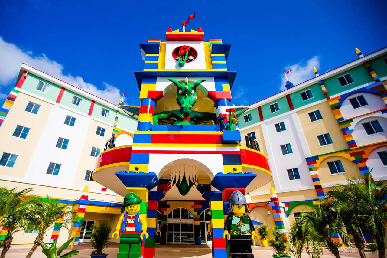 Legoland 桌布 壁紙 — 充滿活力的樂高主題飯店入口，色彩繽紛的積木建築、綠色巨龍雕像和樂高人偶，在清澈的藍天下。