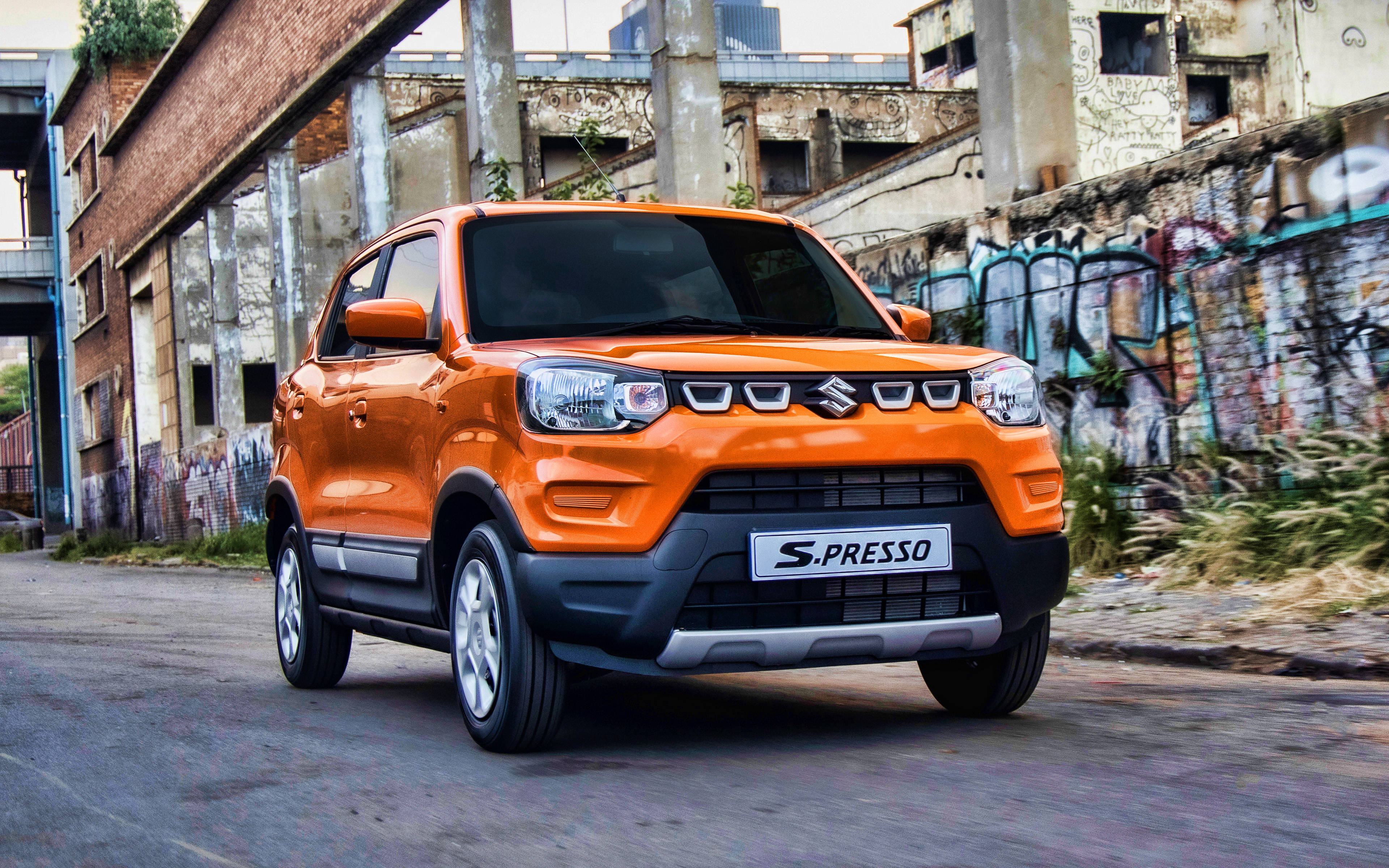 Suzuki 桌布 壁紙 — 充滿活力的橘色鈴木 S-Presso SUV 停放在一條佈滿灰塵的都市街道上，旁邊是佈滿塗鴉的牆壁和破舊的磚造建築。