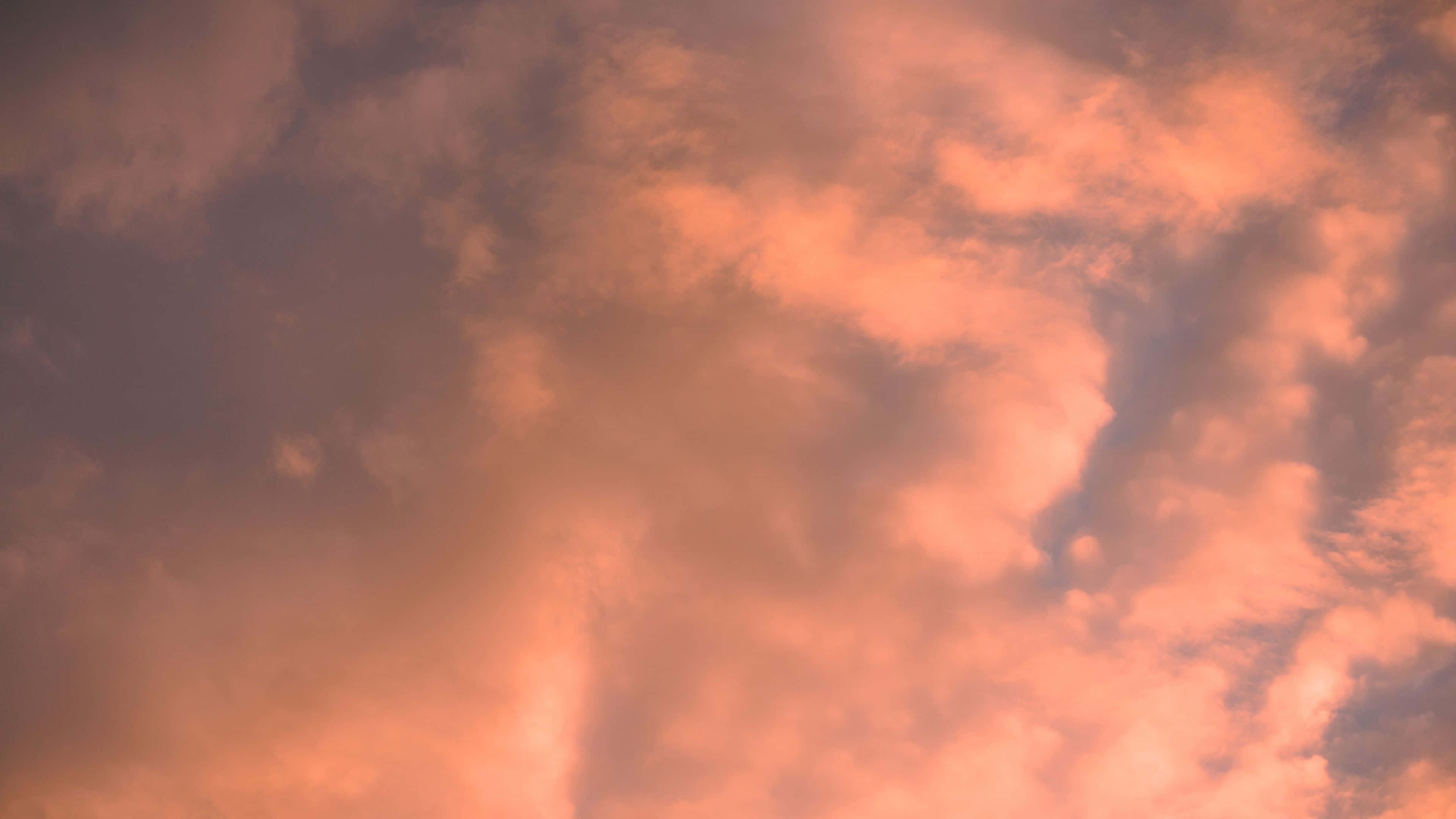 美學雲朵 桌布 壁紙 — 充滿活力的橙色和粉紅色雲朵在暮色天空中戲劇性地旋轉，帶有柔和漸變和紋理縷縷。