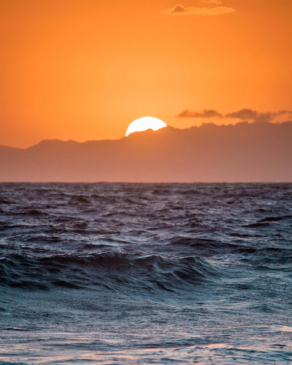 太陽 桌布 壁紙 — 充滿活力的橙色夕陽在遠山背後發光，波浪在深藍色的海洋上泛起漣漪。