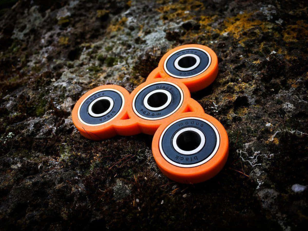 Fidget 桌布 壁紙 — 充滿活力的橙色指尖陀螺帶有黑色軸承，放置在長滿苔蘚的紋理岩石表面上。
