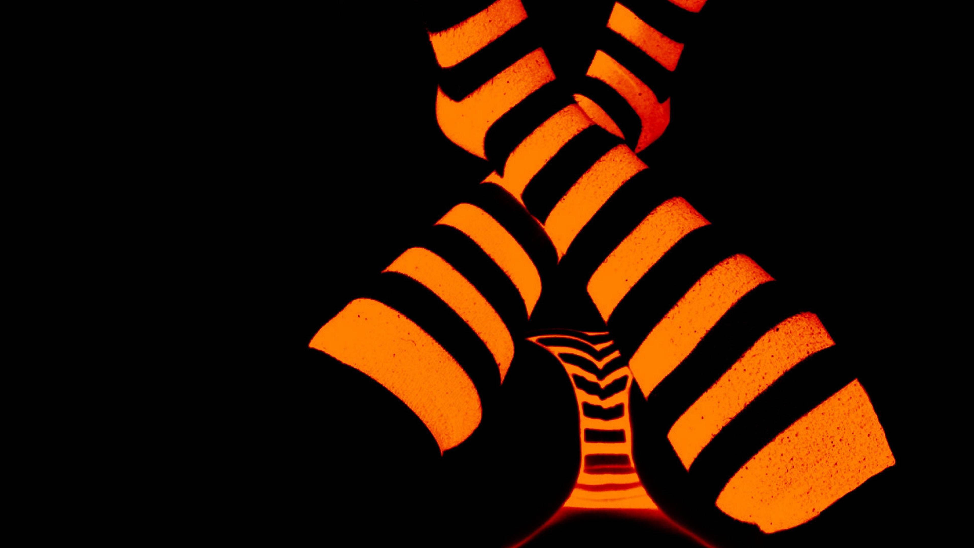 Neon Orange 桌布 壁紙 — 充滿活力的橙色發光條紋管在帶有紋理表面的漆黑背景上形成 X 形狀。