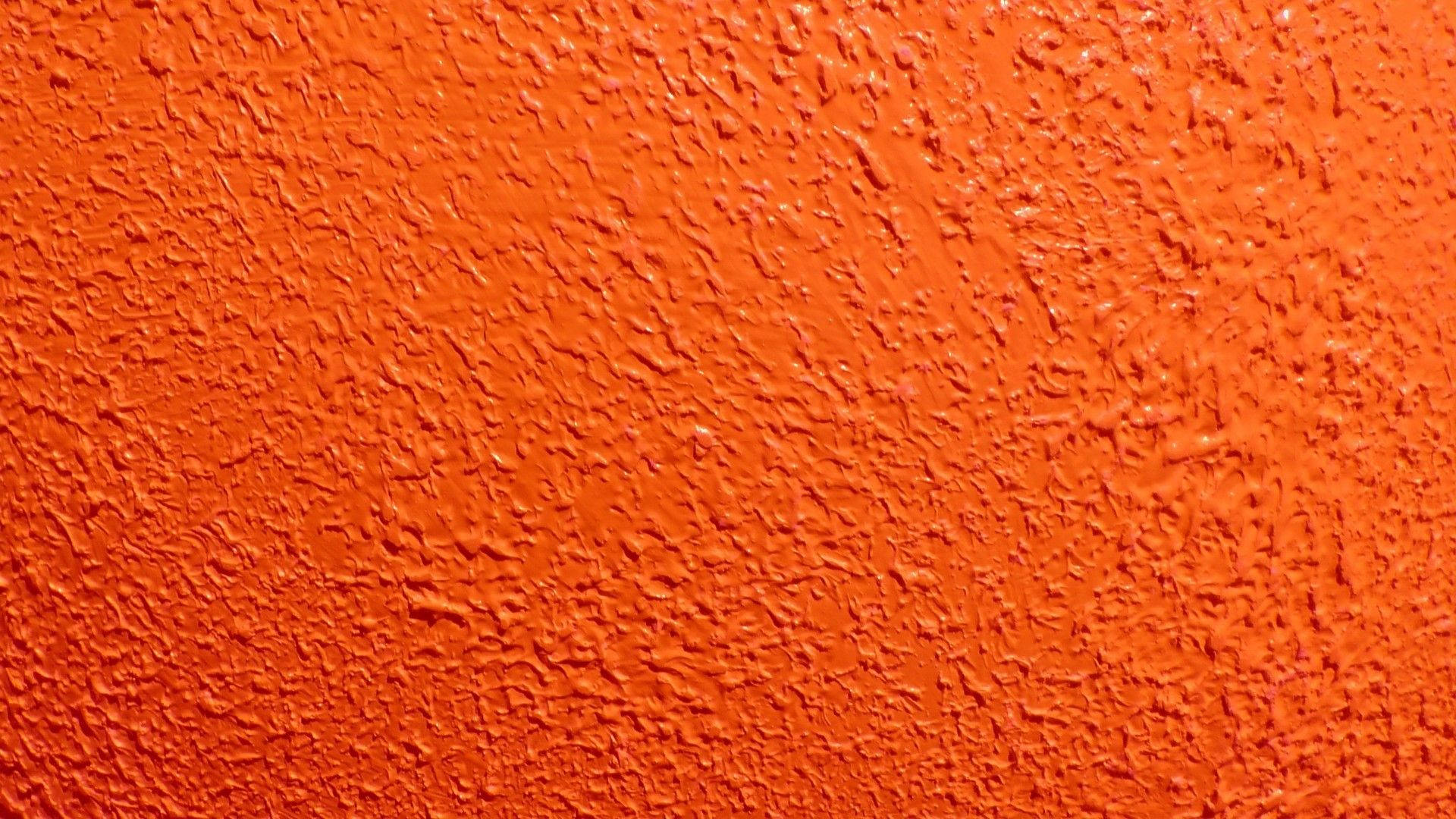 Neon Orange 桌布 壁紙 — 充滿活力的橙色紋理牆壁，在明亮燈光下呈現粗糙剝落的油漆表面。