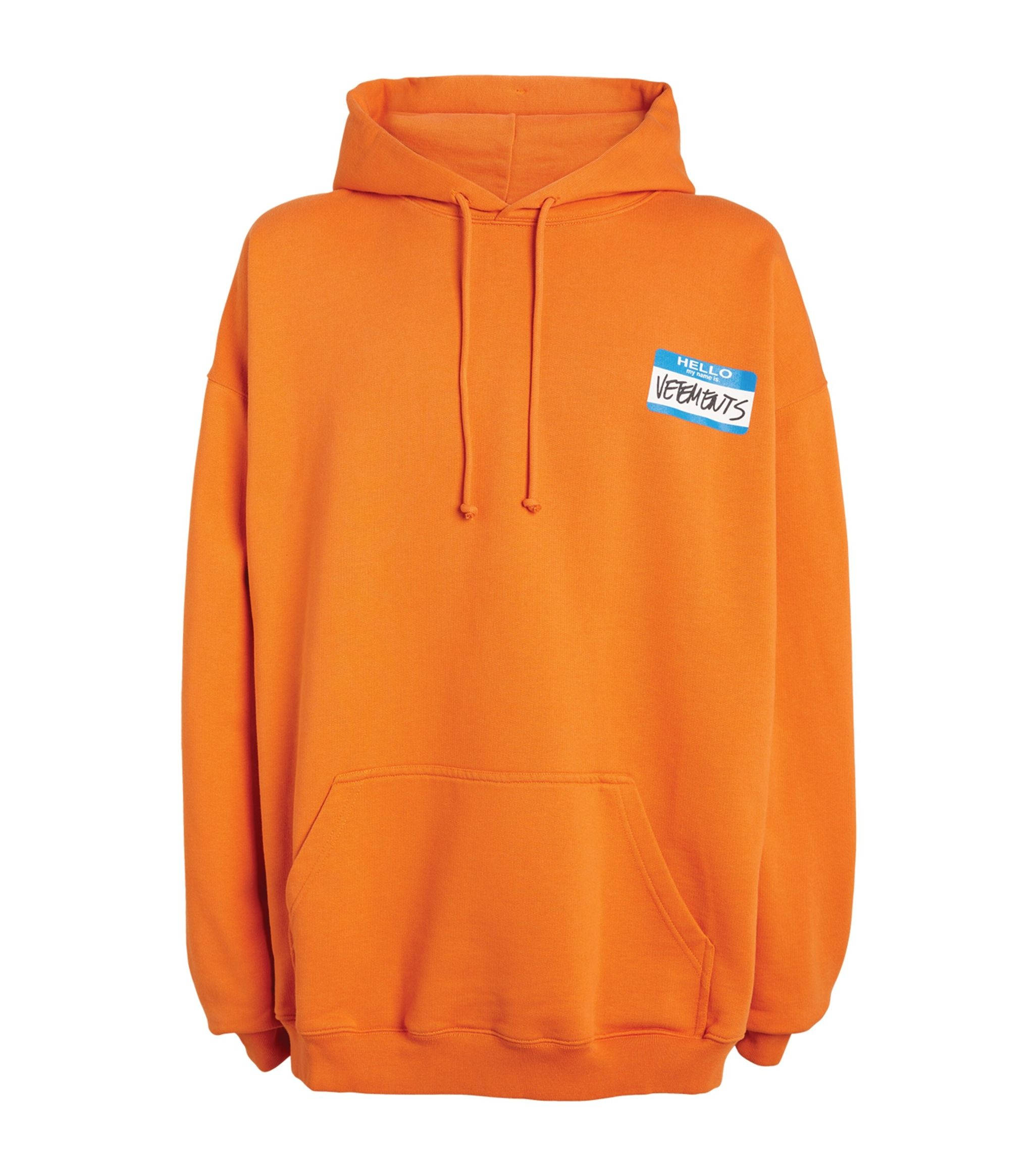 Vetements 桌布 壁紙 — 充滿活力的橙色連帽衫，左胸有一個藍白相間的名牌，上面寫著「HELLO VEEP BUTS」。