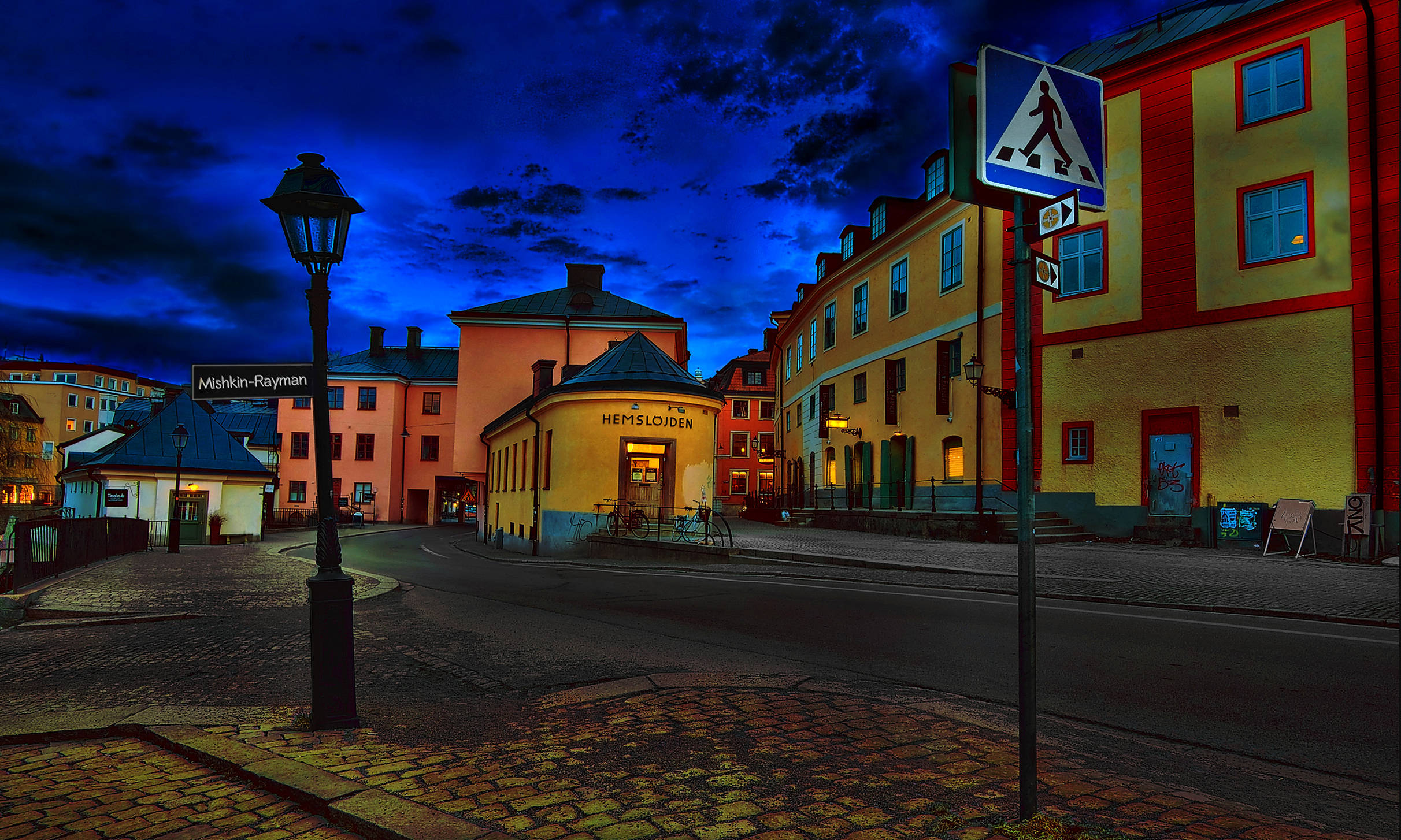 Sweden 桌布 壁紙 — 充滿活力的歐洲街道在黃昏時分，色彩繽紛的建築物、鵝卵石路面和發光的窗戶，在深藍色的天空下。