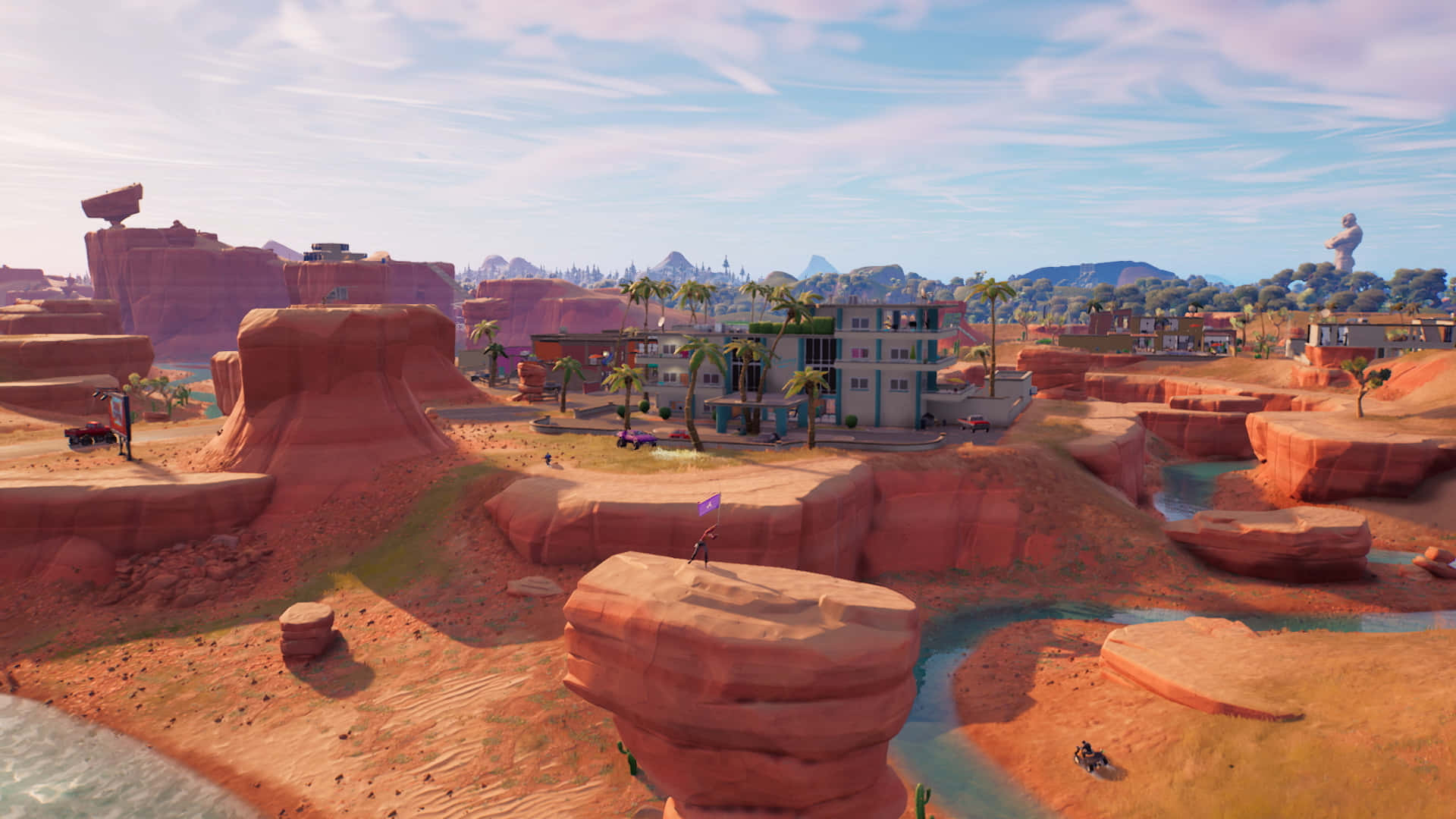 Fortnite Chapter 3 桌布 壁紙 — 充滿活力的沙漠景觀，有紅色岩層和一座色彩繽紛的建築物，坐落在棕櫚樹之間，上方是明亮的藍天。
