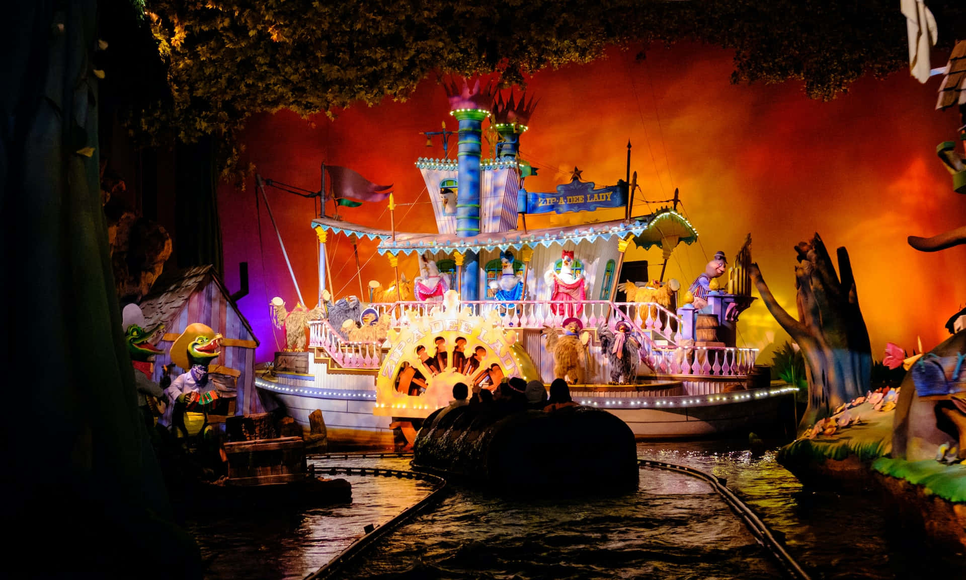 Splash Mountain 桌布 壁紙 — 充滿活力的河船之旅，色彩繽紛的角色和發光的燈光，背景是火熱的橙色。