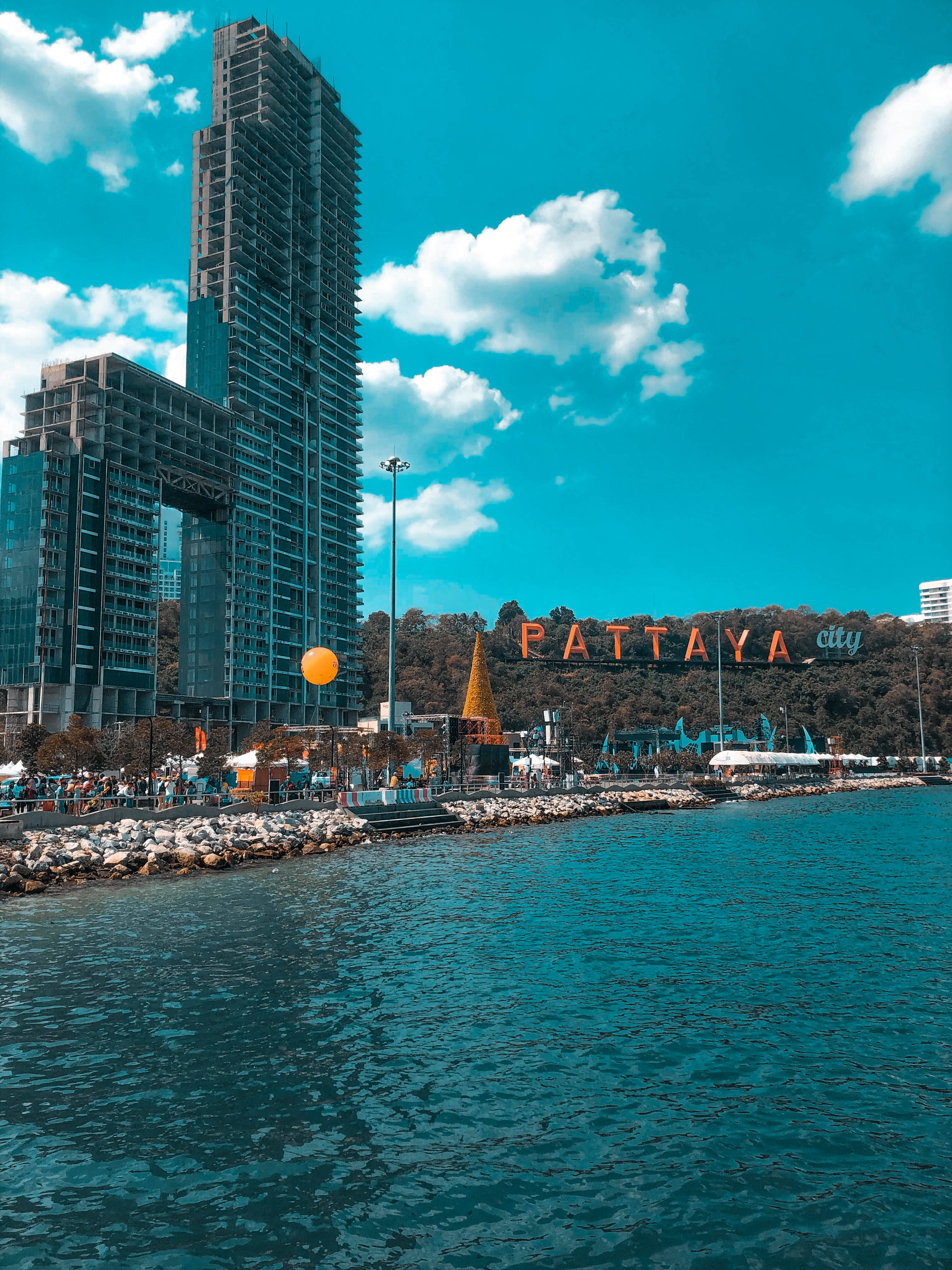 Skyscraper 桌布 壁紙 — 充滿活力的沿海城市景觀，一座高聳的玻璃摩天大樓矗立在碧綠的海水旁，天空湛藍，白雲朵朵。