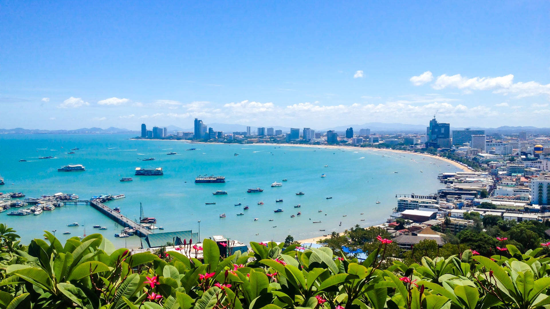城市 桌布 壁紙 — 充滿活力的沿海城市景觀，碧綠的海水點綴著船隻，沙灘在明亮的藍天下蜿蜒。