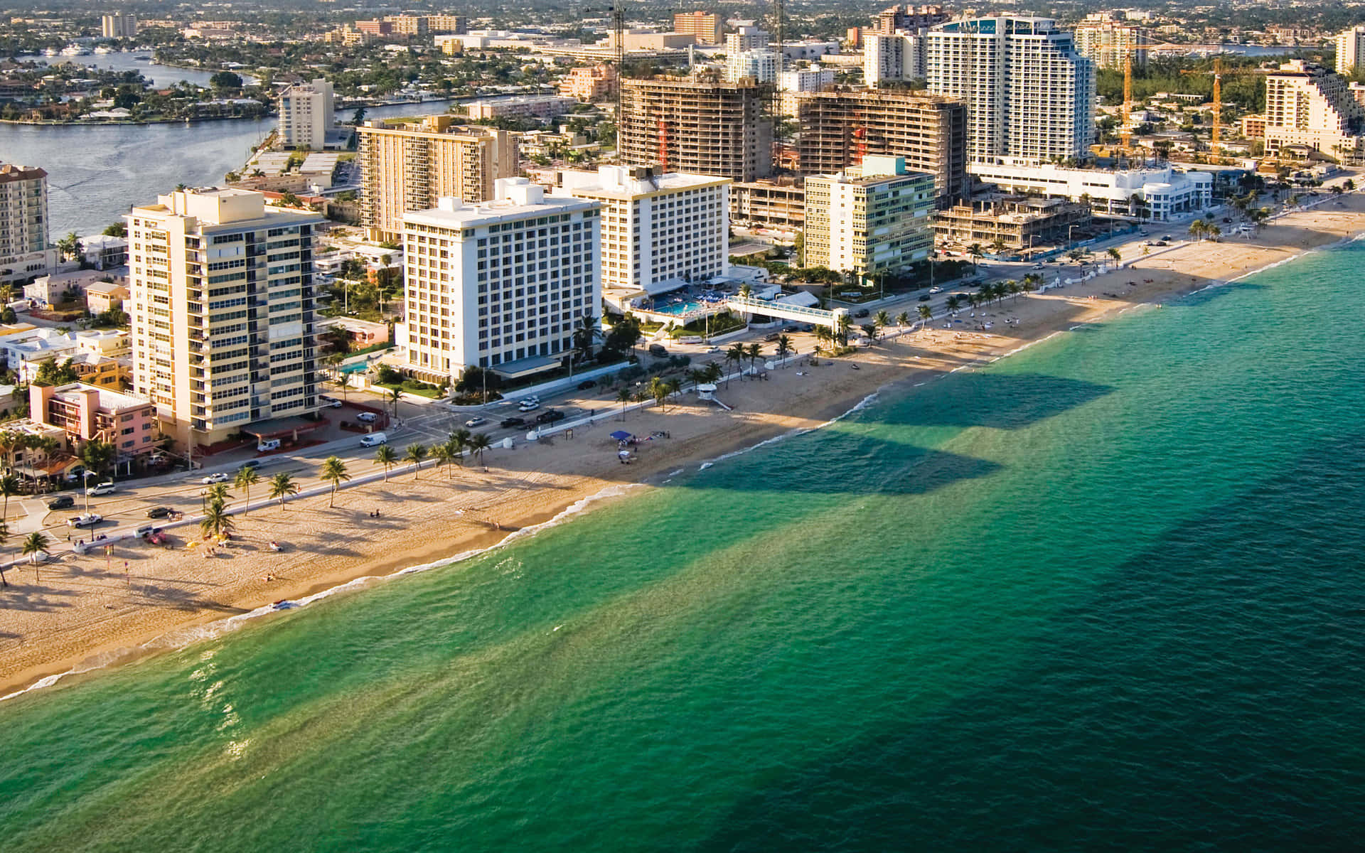 florida 桌布 壁紙 — 充滿活力的沿海城市景觀鳥瞰圖，碧綠的海水拍打著沙灘，沙灘上種滿棕櫚樹和現代化高層酒店。