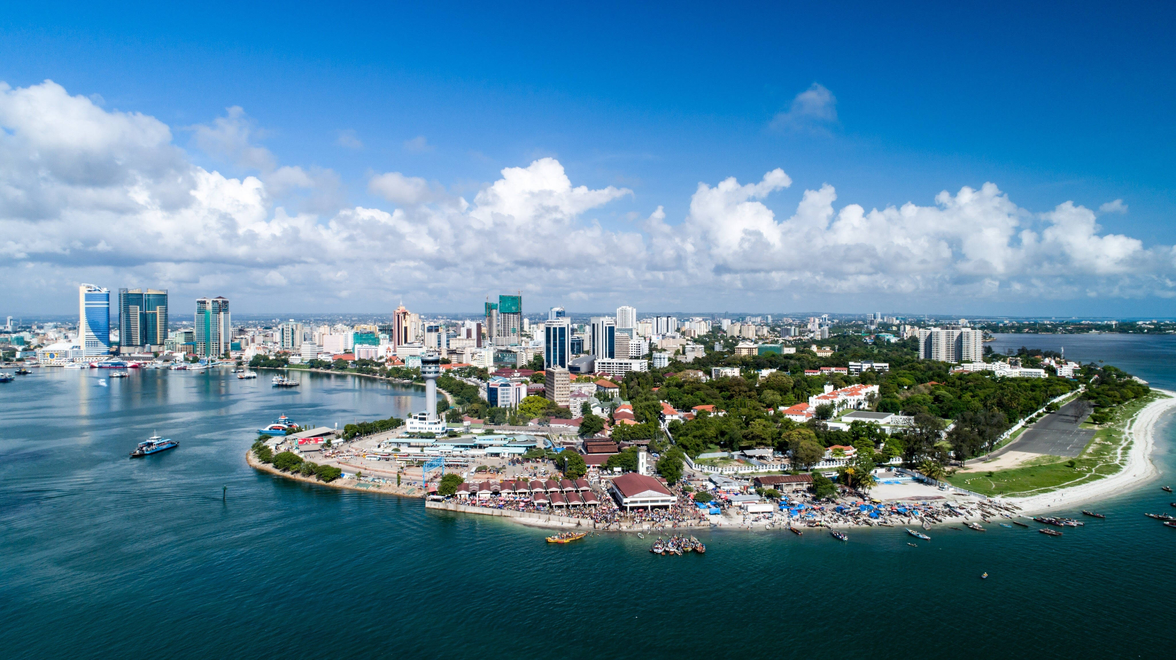 Tanzania 桌布 壁紙 — 充滿活力的沿海城市的鳥瞰圖，擁有現代摩天大樓和繁華的島嶼海灘，在明亮的藍天和蓬鬆的雲彩下。
