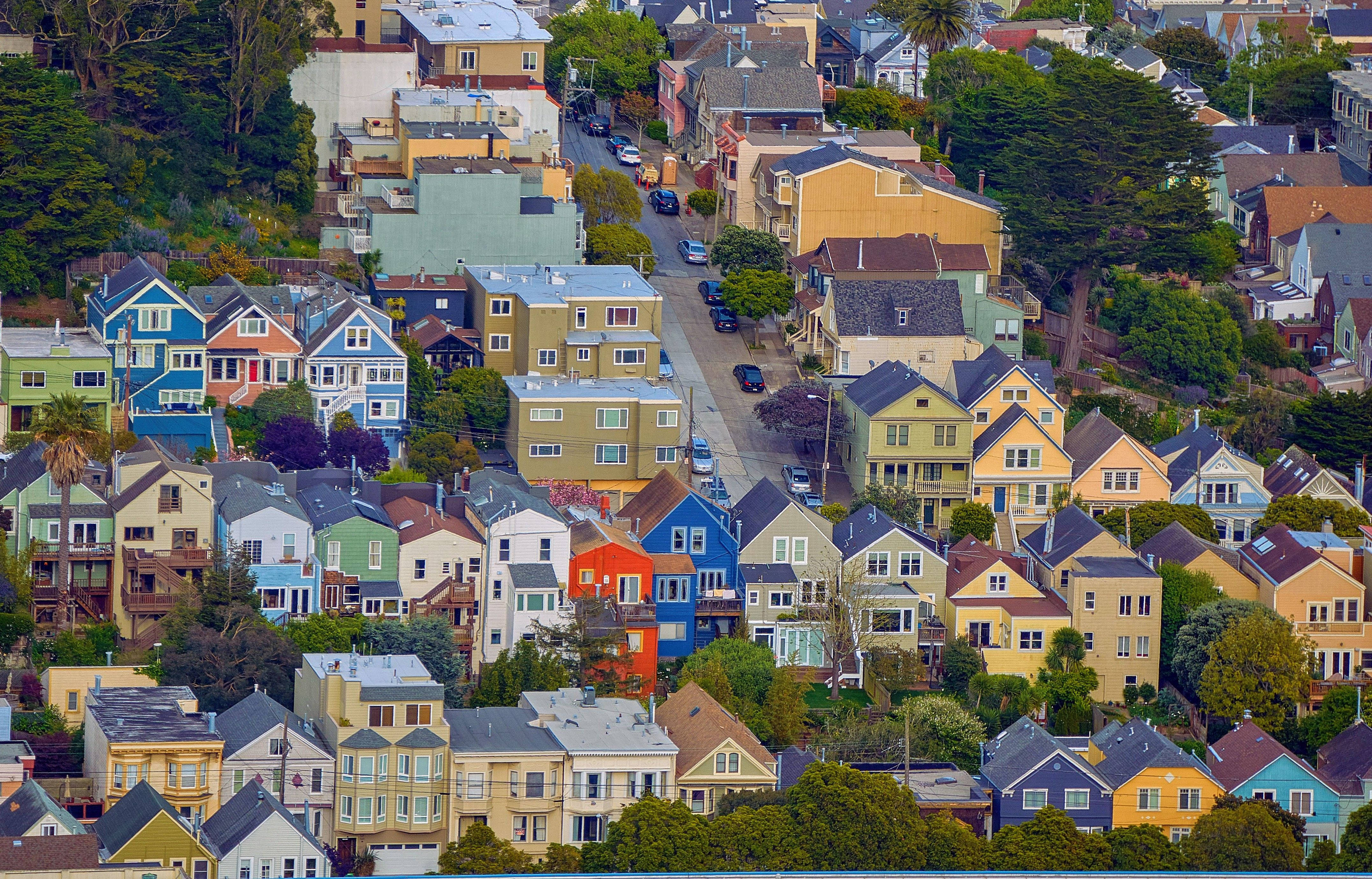 San Francisco 桌布 壁紙 — 充滿活力的沿海小鎮中，色彩繽紛的維多利亞式房屋沿著綠樹成蔭的山坡層疊而下的鳥瞰圖。