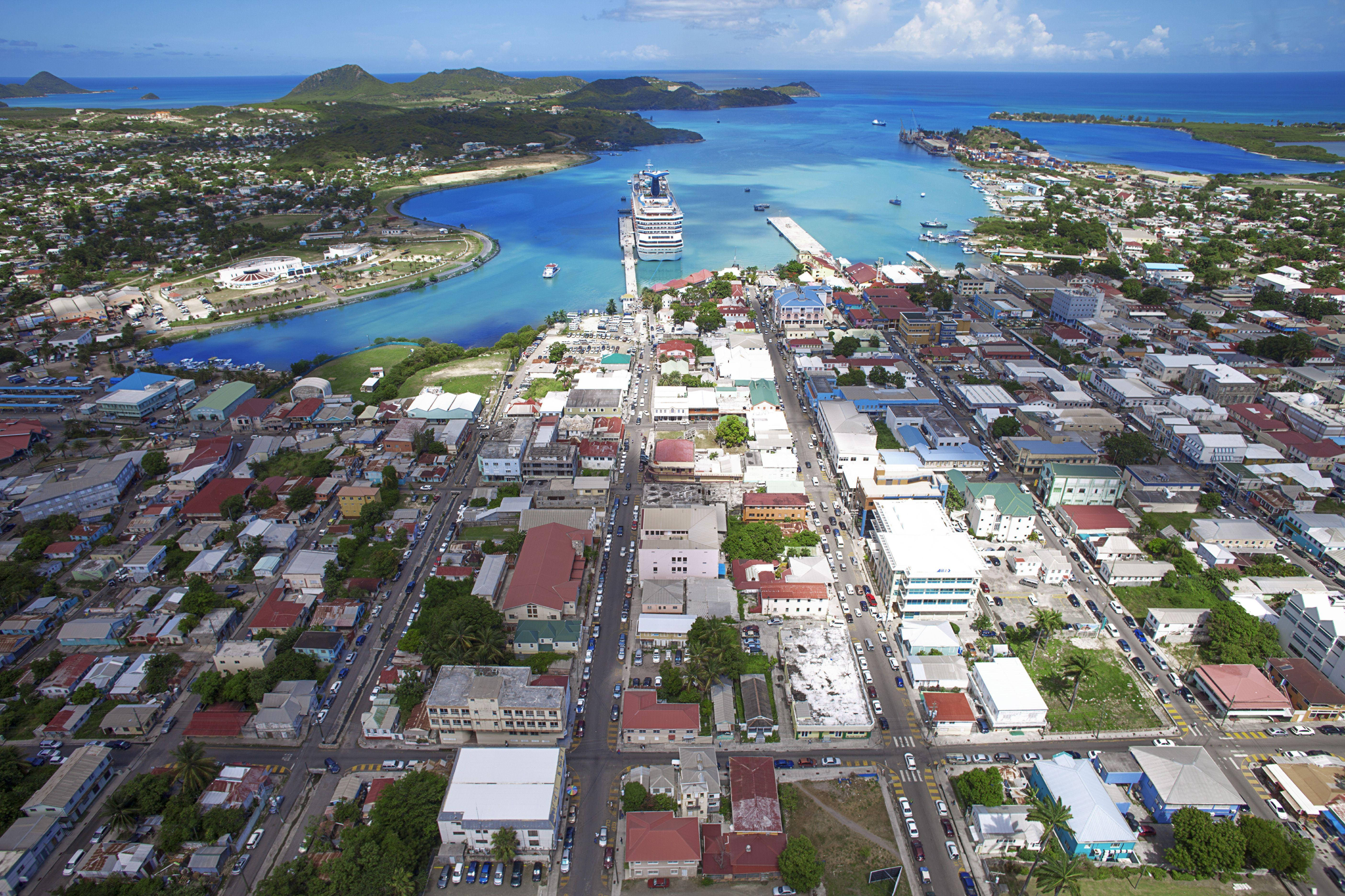 Caribbean 桌布 壁紙 — 充滿活力的沿海小鎮鳥瞰圖，擁有色彩繽紛的建築物、蜿蜒的街道，以及停泊在碧綠海水中的大型郵輪。