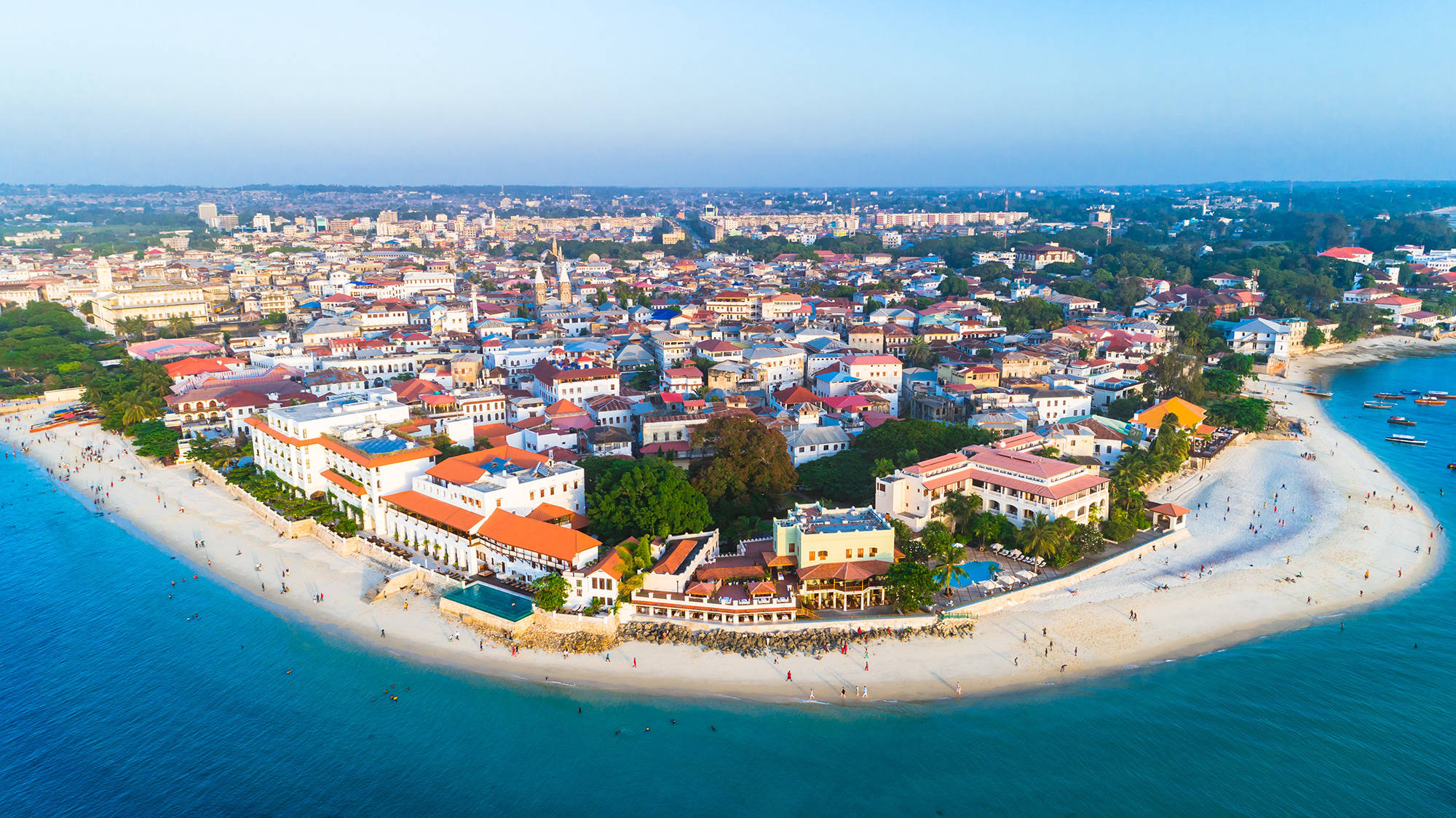 Tanzania 桌布 壁紙 — 充滿活力的沿海小鎮鳥瞰圖，色彩繽紛的建築依偎在沙灘和碧綠海水旁。