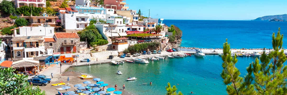 Greek Island 桌布 壁紙 — 充滿活力的沿海村莊，白色建築沿懸崖層疊而下，通往停滿船隻和享受日光浴的碧綠海灣。