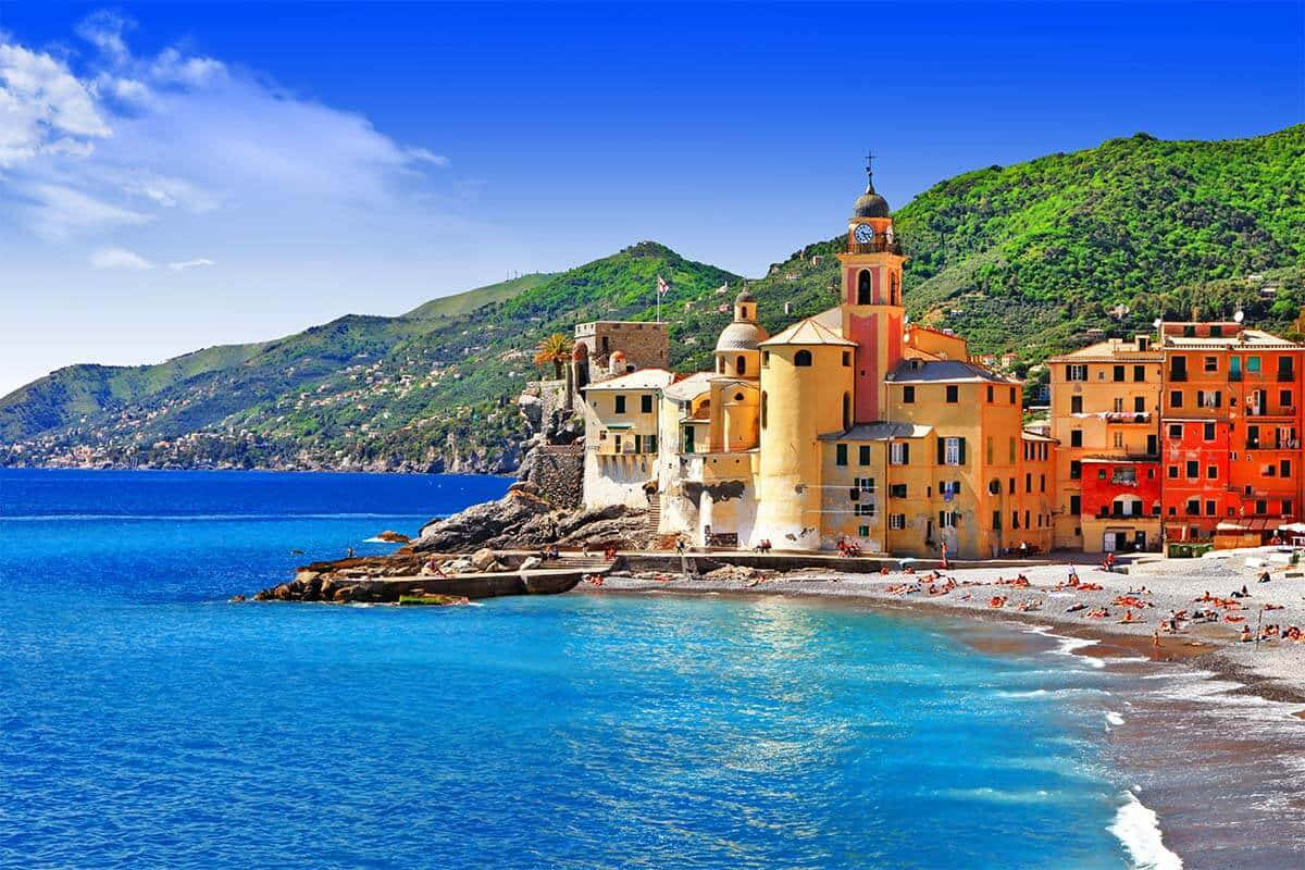 Italian Island 桌布 壁紙 — 充滿活力的沿海村莊，赤陶建築坐落在懸崖上，俯瞰著碧綠的海水和翠綠的山丘，頭頂是明亮的藍天。