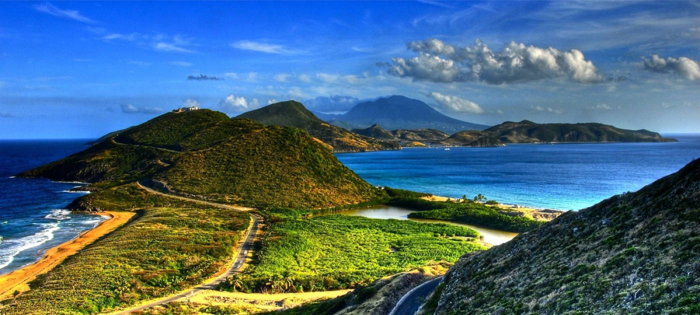 山景 桌布 壁紙 — 充滿活力的海岸景觀，蜿蜒的道路環繞著鬱鬱蔥蔥的綠色山丘和碧綠的海水，在明亮的藍天下有蓬鬆的雲朵。