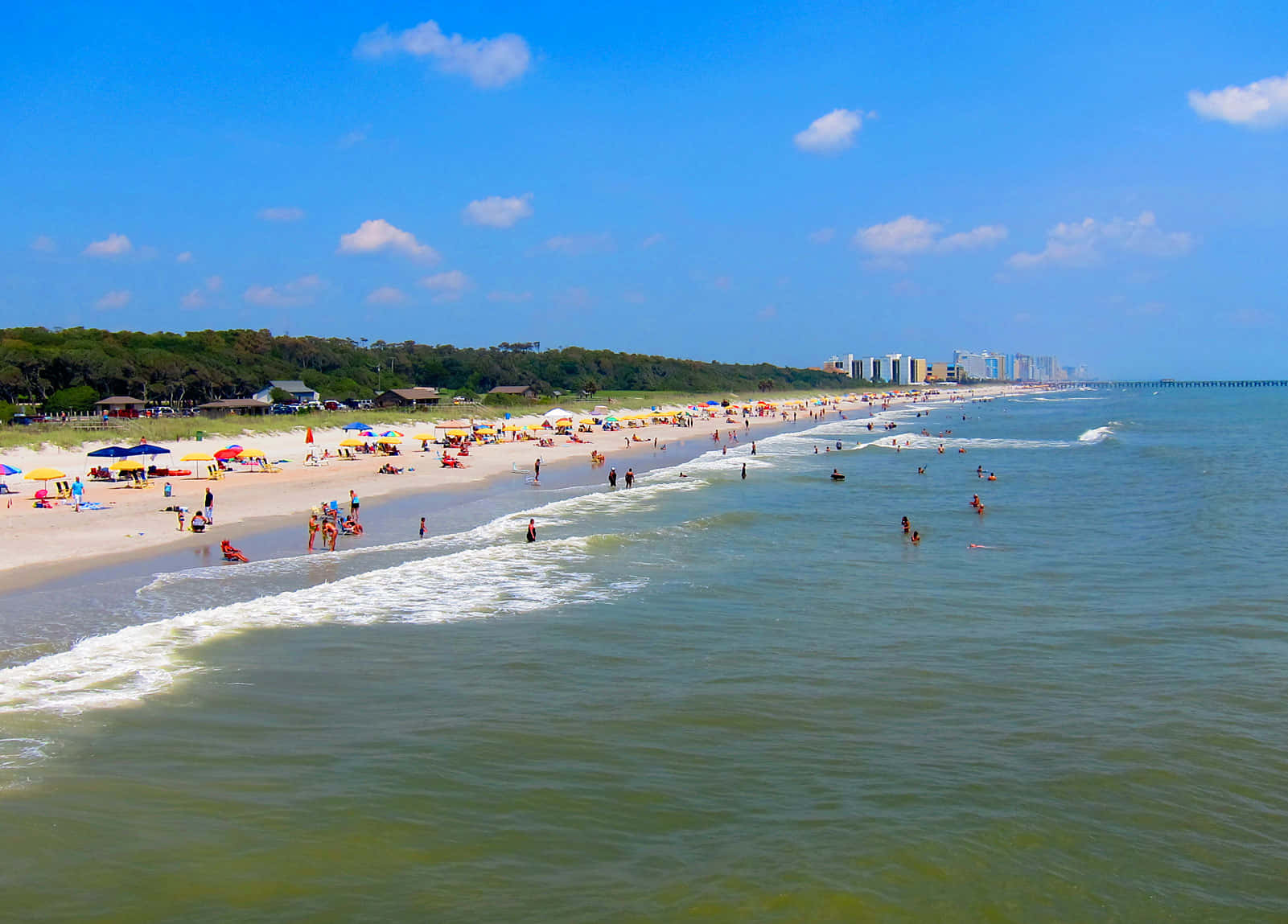 Myrtle Beach 桌布 壁紙 — 充滿活力的海灘場景，碧綠的海浪拍打著擁擠的沙灘，上方是晴朗的藍天，點綴著蓬鬆的白雲。