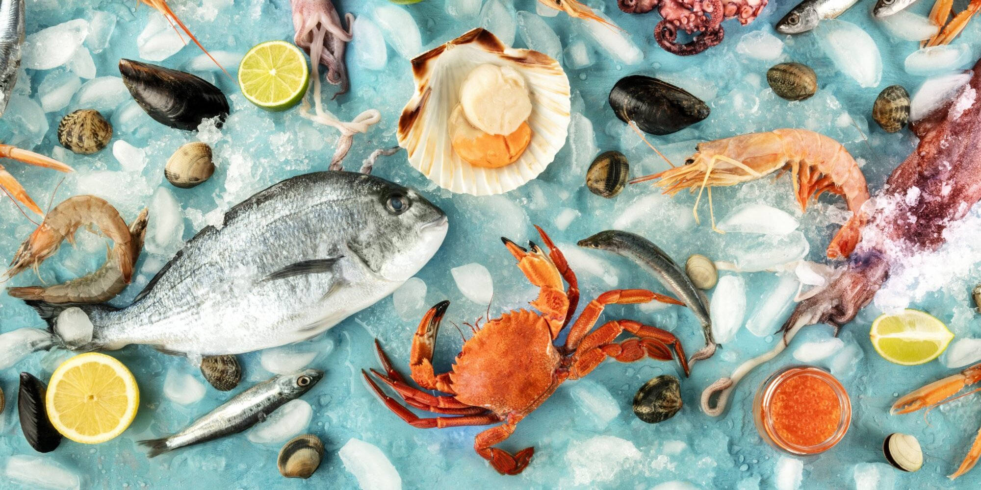 Seafood 桌布 壁紙 — 充滿活力的海鮮拼盤，包括整條魚、蟹、蝦和蛤蜊，放在藍色冰上，配以檸檬角和貝殼。