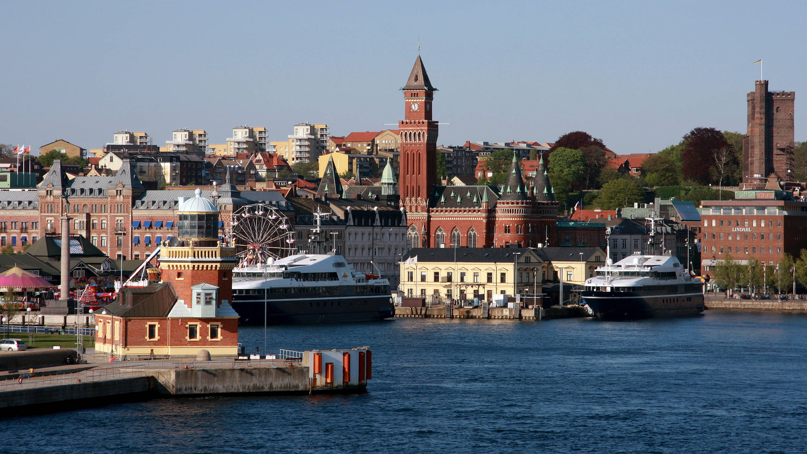 Sweden 桌布 壁紙 — 充滿活力的港口城市景觀，擁有歷史悠久的紅磚建築、鐘樓和停泊在晴朗藍天下的渡輪。