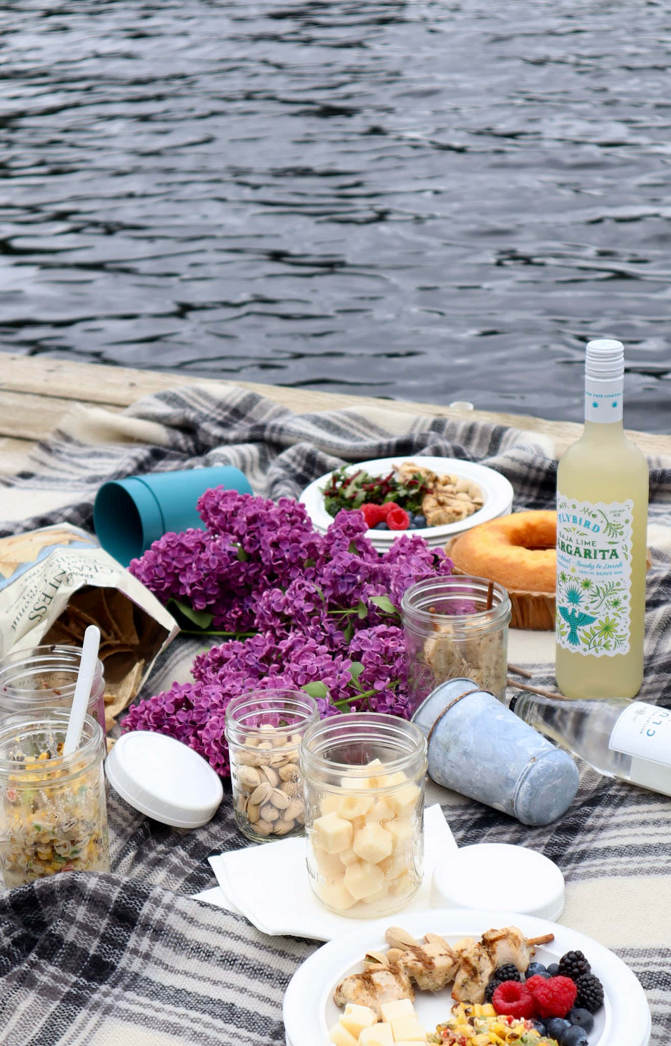 Beach Picnic 桌布 壁紙 — 充滿活力的湖邊野餐，有紫色丁香花、烤雞和瑪格麗特酒，鋪在格紋毯上。