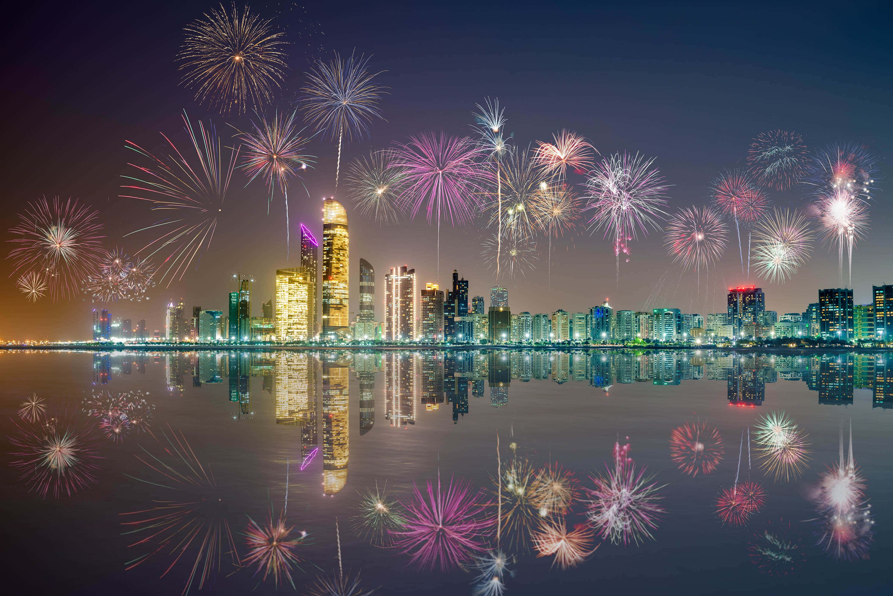 彩色動圖 桌布 壁紙 — 充滿活力的煙火在夜晚平靜的水面上反射出閃爍的城市天際線上空爆炸。