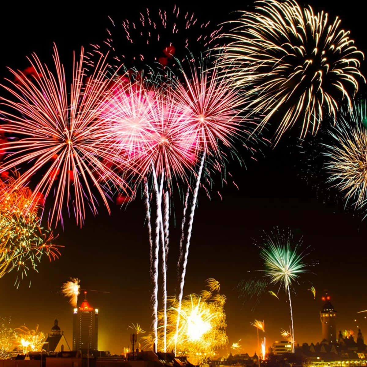 Fireworks 桌布 壁紙 — 充滿活力的煙火在夜間城市天際線上綻放出耀眼的紅色、金色和綠色。