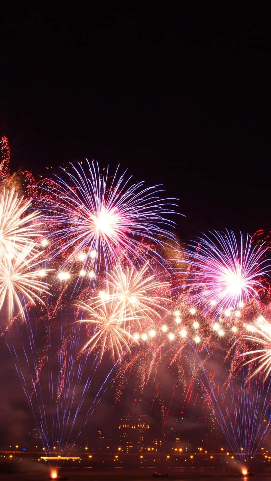 Fireworks 桌布 壁紙 — 充滿活力的煙火在夜間的城市天際線上綻放出耀眼的紅色、紫色和白色。