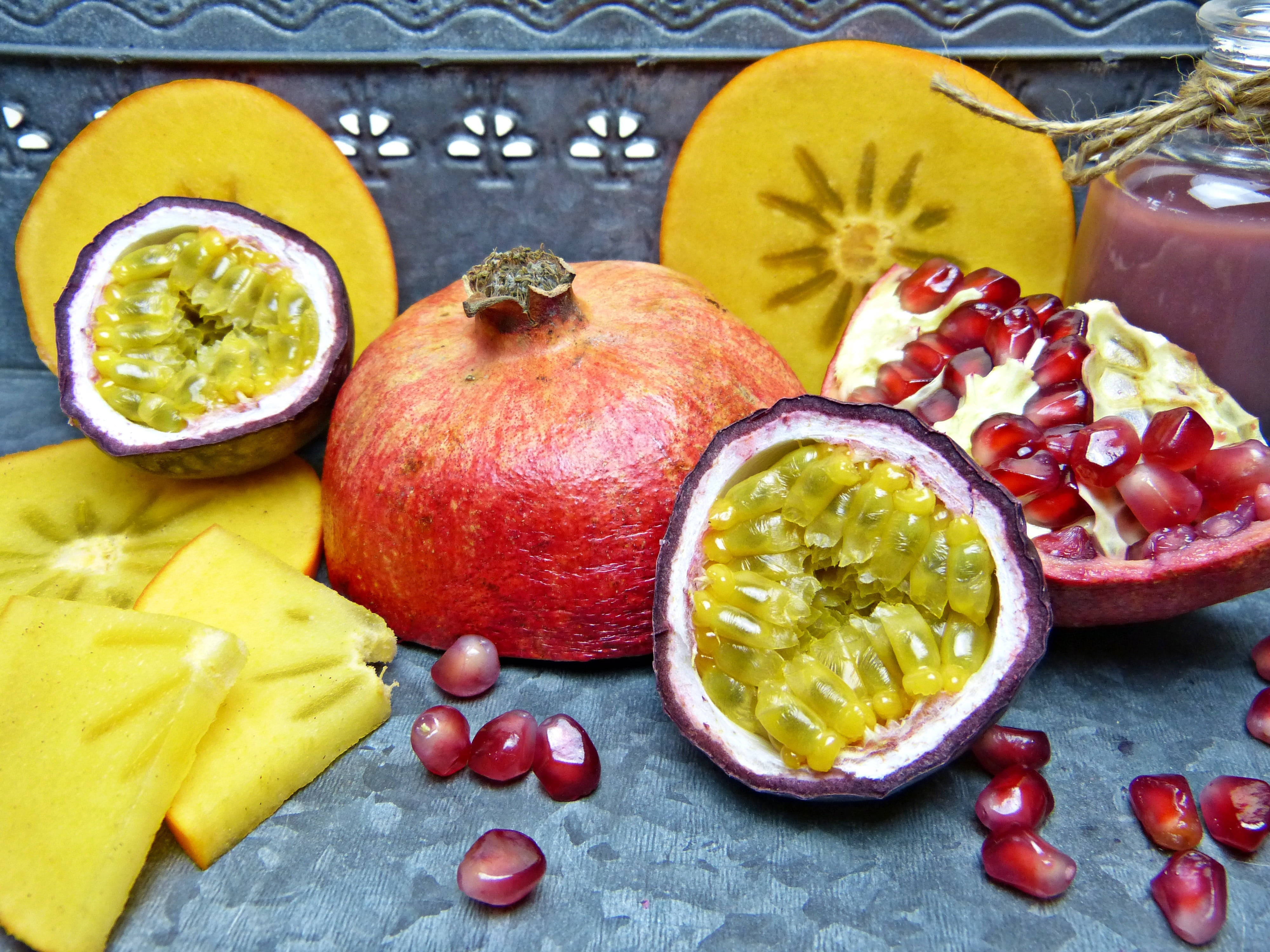 Pomegranate 桌布 壁紙 — 充滿活力的熱帶水果，包括石榴、百香果和黃色楊桃，排列在帶紋理的金屬托盤上。