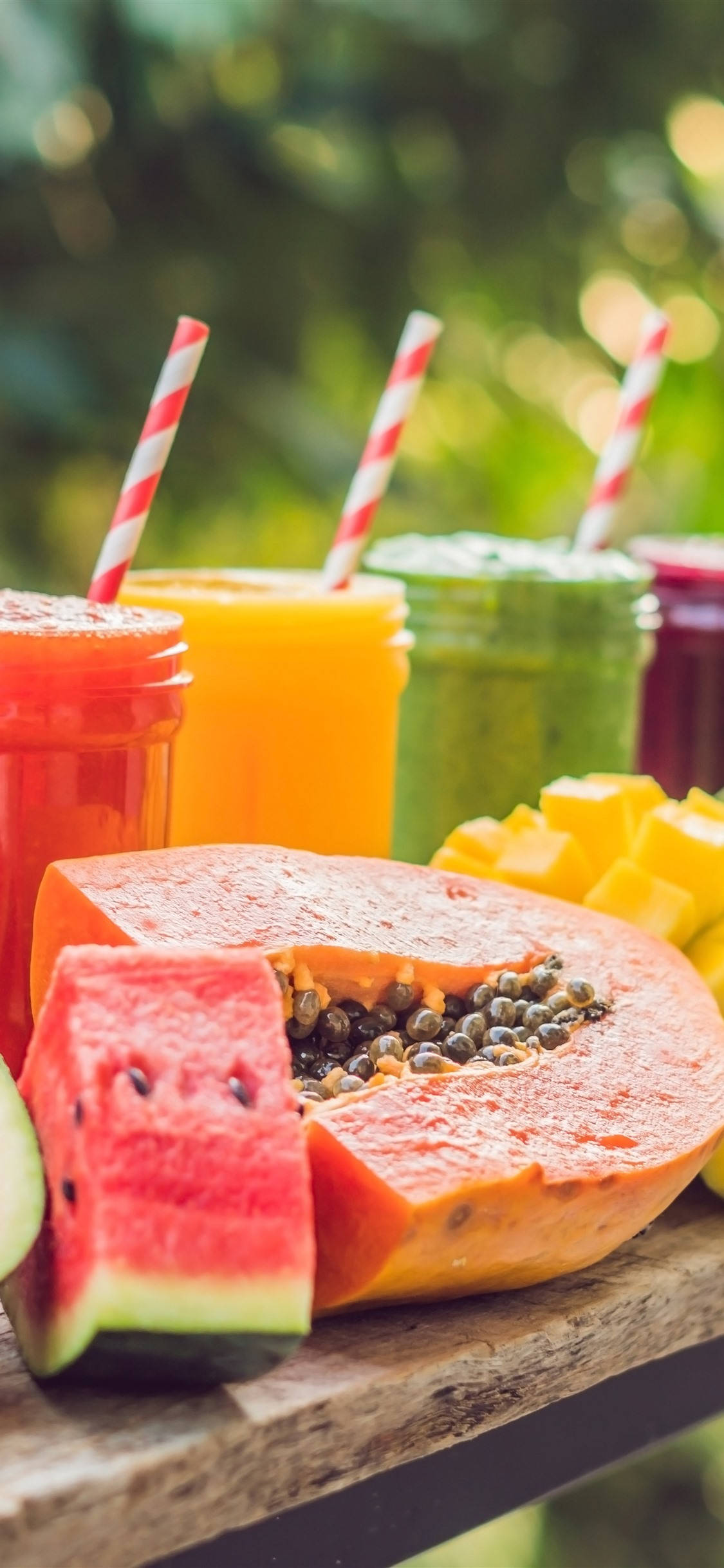 Smoothie 桌布 壁紙 — 充滿活力的熱帶水果冰沙裝在玻璃罐中，配上條紋吸管，與新鮮木瓜、西瓜和芒果一起放在質樸的木桌上。