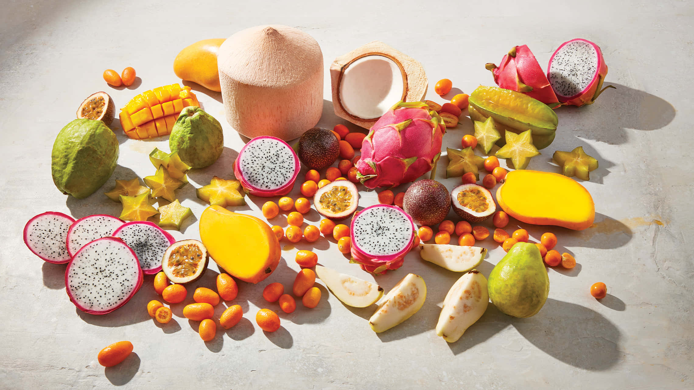 Fruit 桌布 壁紙 — 充滿活力的熱帶水果拼盤，包括火龍果、芒果、楊桃和椰子，排列在紋理混凝土表面上，在明亮的陽光下。