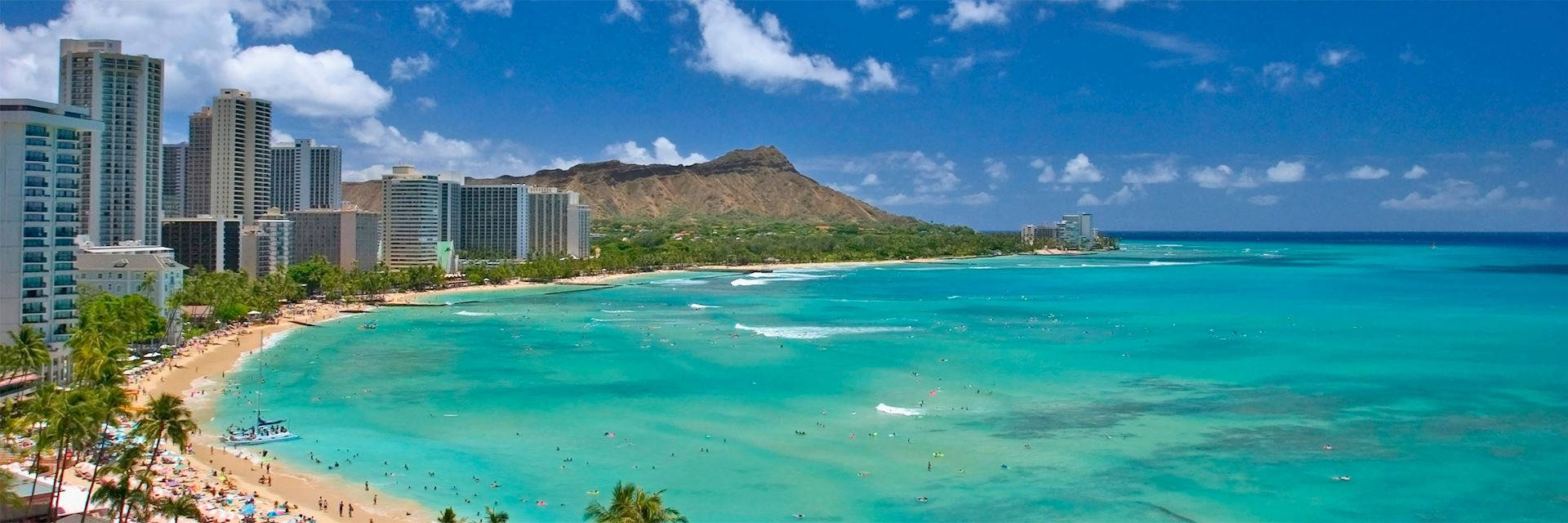 夏威夷 桌布 壁紙 — 充滿活力的熱帶海灘場景，有碧綠的海水、沙灘、棕櫚樹，以及現代高樓大廈和標誌性火山山峰在明亮藍天下的背景。