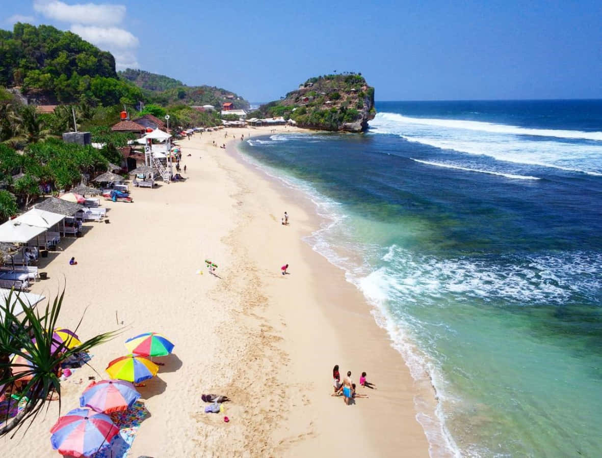 Vacation Mode 桌布 壁紙 — 充滿活力的熱帶海灘鳥瞰圖，碧綠的海水拍打著金色沙灘，沙灘上點綴著色彩繽紛的遮陽傘和遊客。