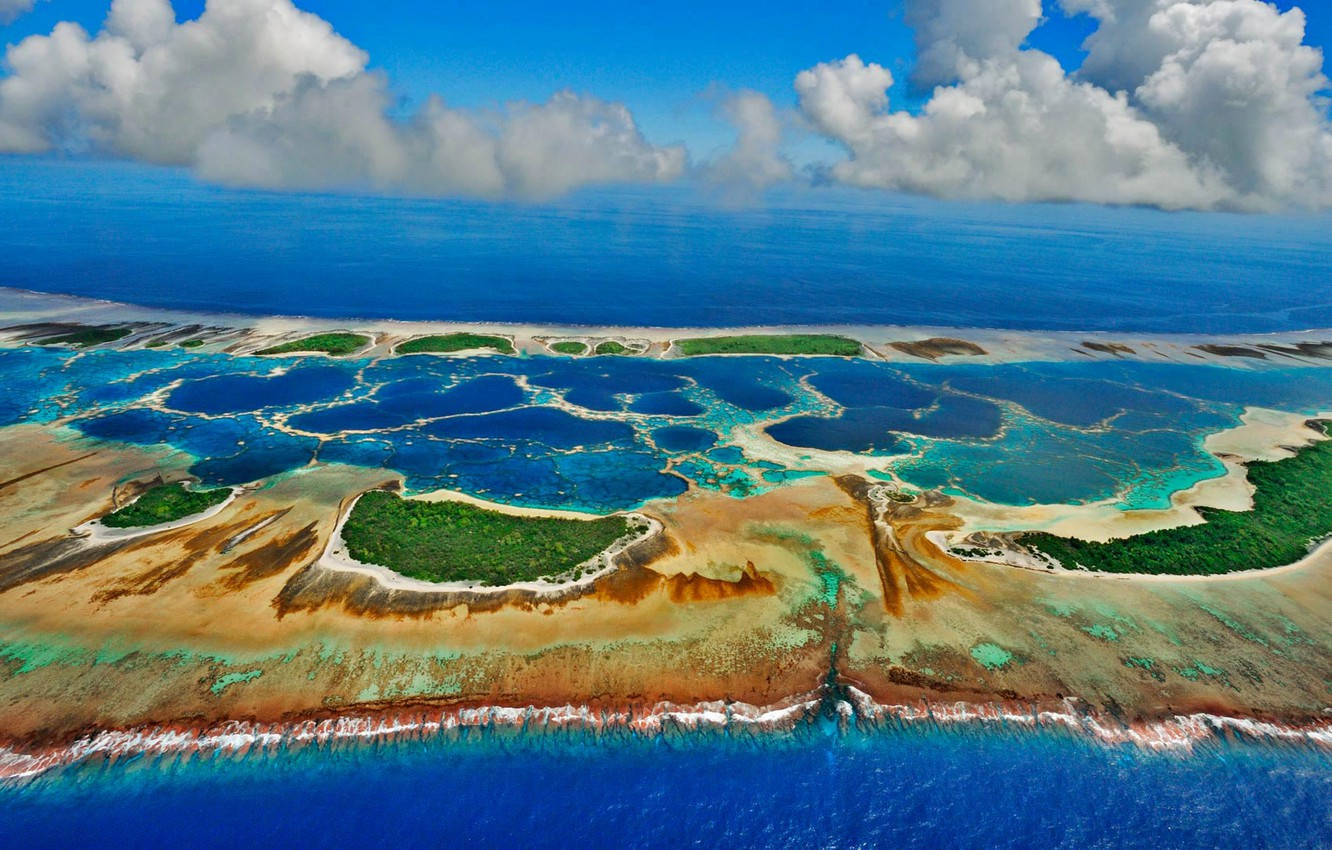 Kiribati 桌布 壁紙 — 充滿活力的珊瑚環礁鳥瞰圖，碧綠色的潟湖被深藍色的海洋和白雲環繞。