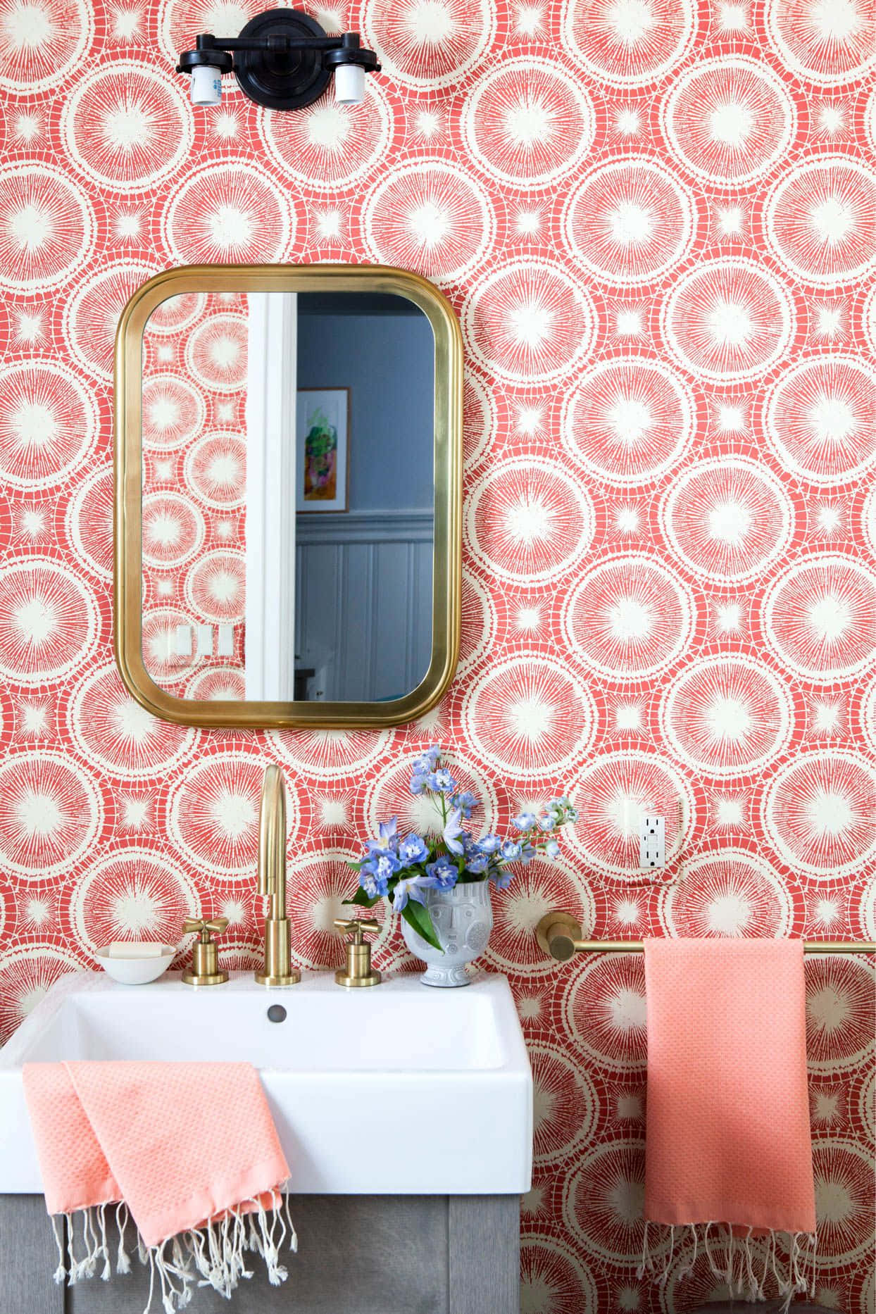 Bathroom Decor 桌布 壁紙 — 充滿活力的珊瑚色浴室，採用幾何圓形壁紙，配有金色鏡框的鏡子和相配的毛巾。