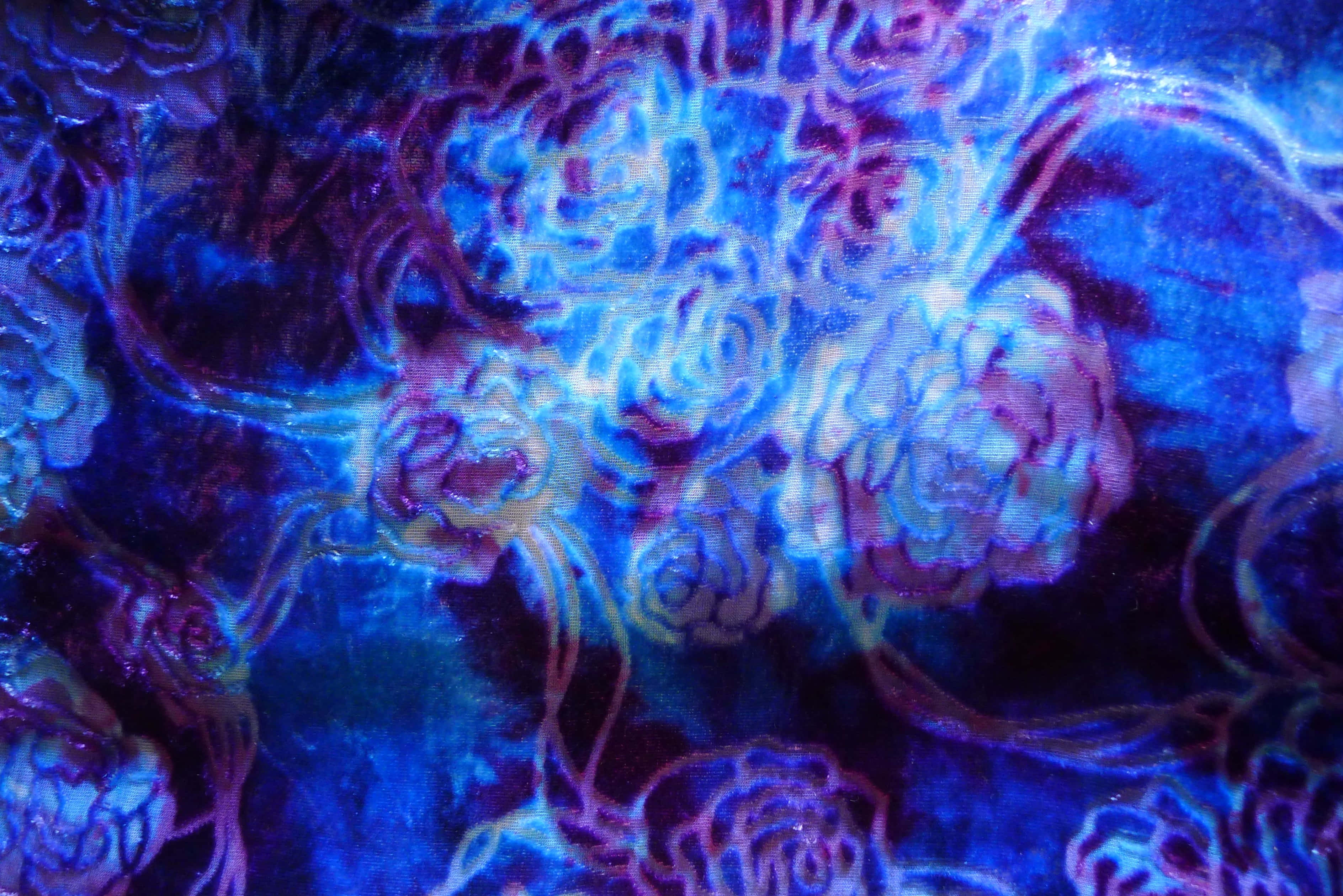 Blue Tie Dye 桌布 壁紙 — 充滿活力的發光藍色和紫色花卉圖案在帶有霓虹亮點的深色紋理表面上旋轉。