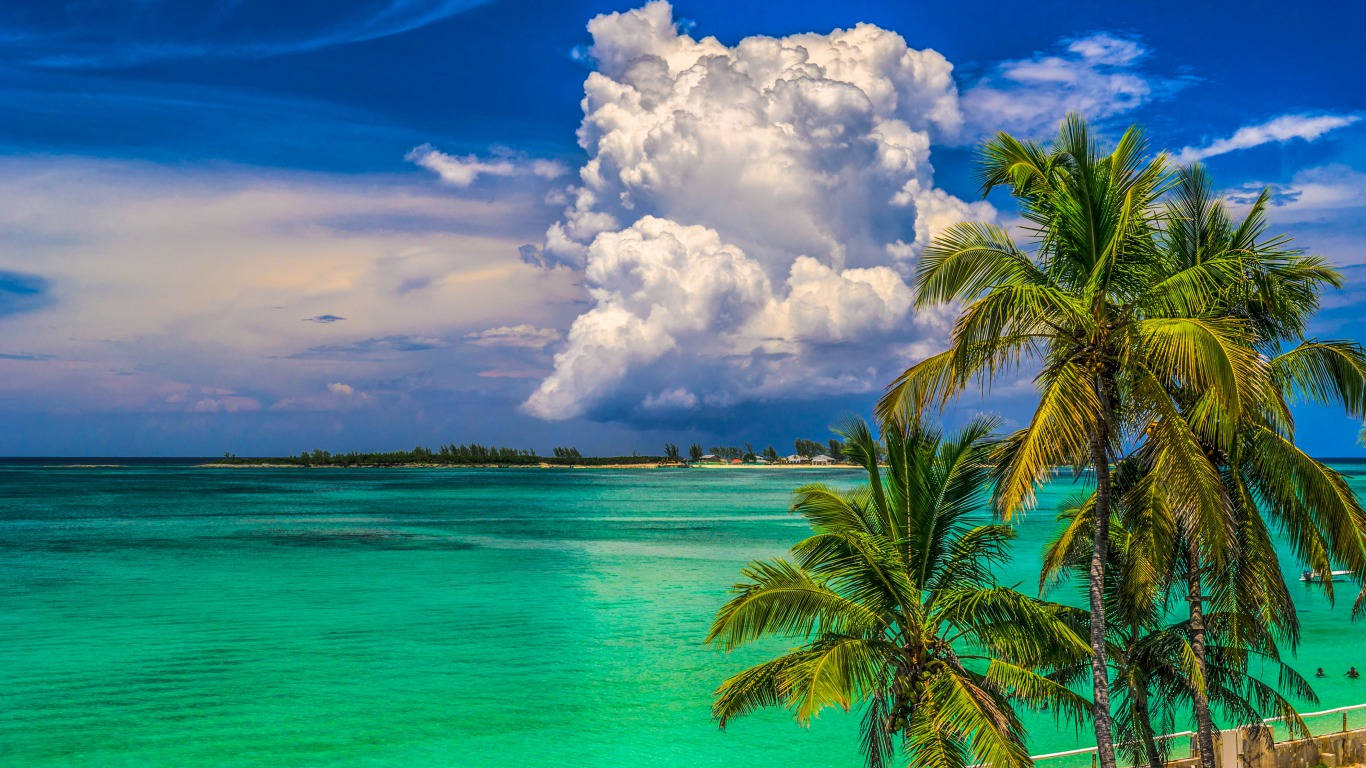 Marshall Island 桌布 壁紙 — 充滿活力的碧綠海水在戲劇性的天空下延伸，蓬鬆的白雲聳立在熱帶島嶼上搖曳的棕櫚樹之上。