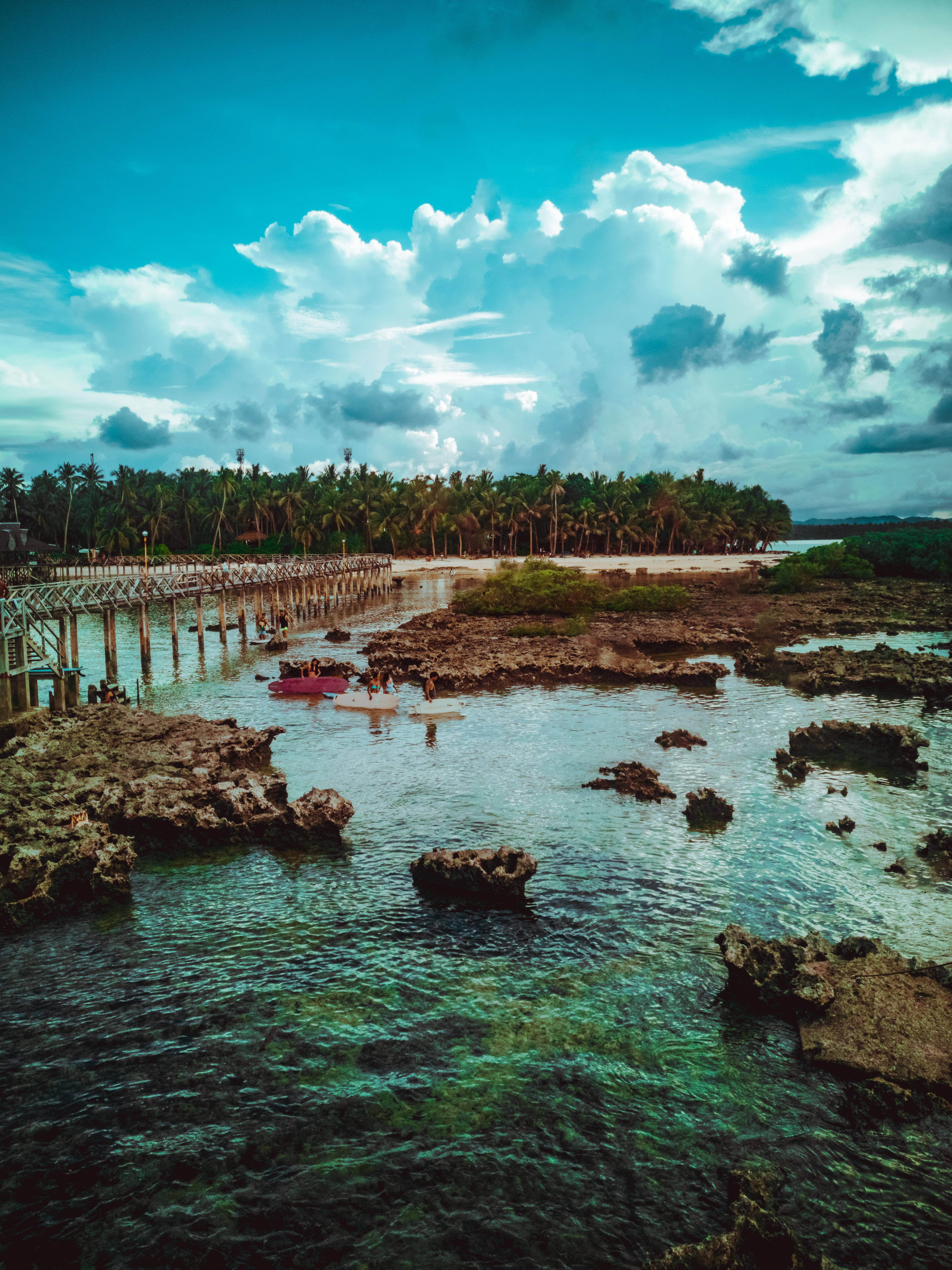 Siargao 桌布 壁紙 — 充滿活力的碧綠海水在珊瑚岩周圍泛起漣漪，下方是戲劇性的天空，熱帶海岸線上方有蓬鬆的白雲。