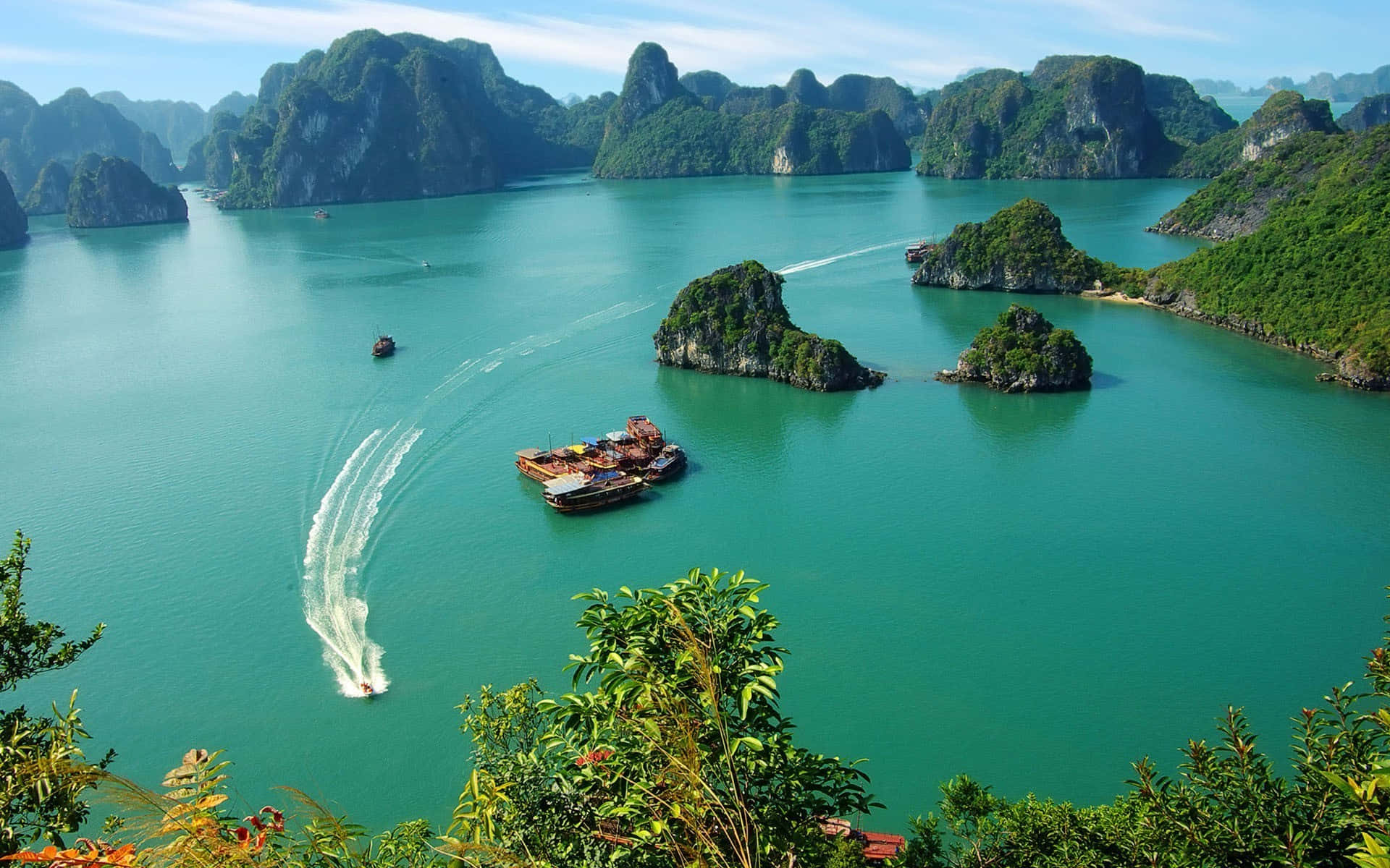 Vietnam 桌布 壁紙 — 充滿活力的碧綠海水懷抱著翠綠的喀斯特島嶼，快艇在寧靜的海灣上劃出白色航跡。