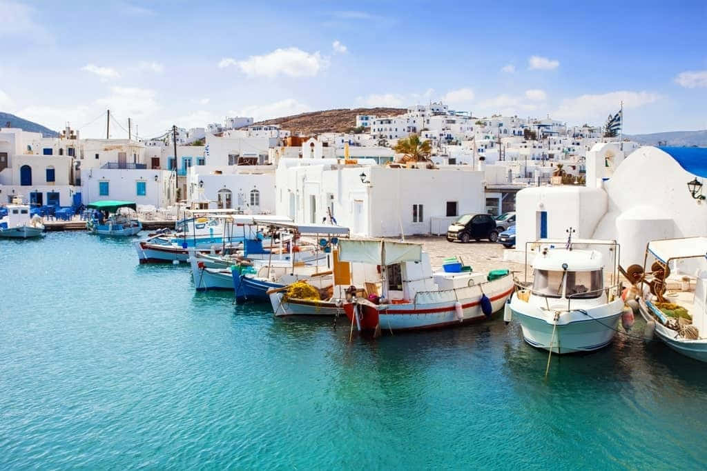 Greek Island 桌布 壁紙 — 充滿活力的碧綠海水懷抱著色彩繽紛的漁船，停泊在陽光明媚的港灣，四周是標誌性的白色希臘建築。