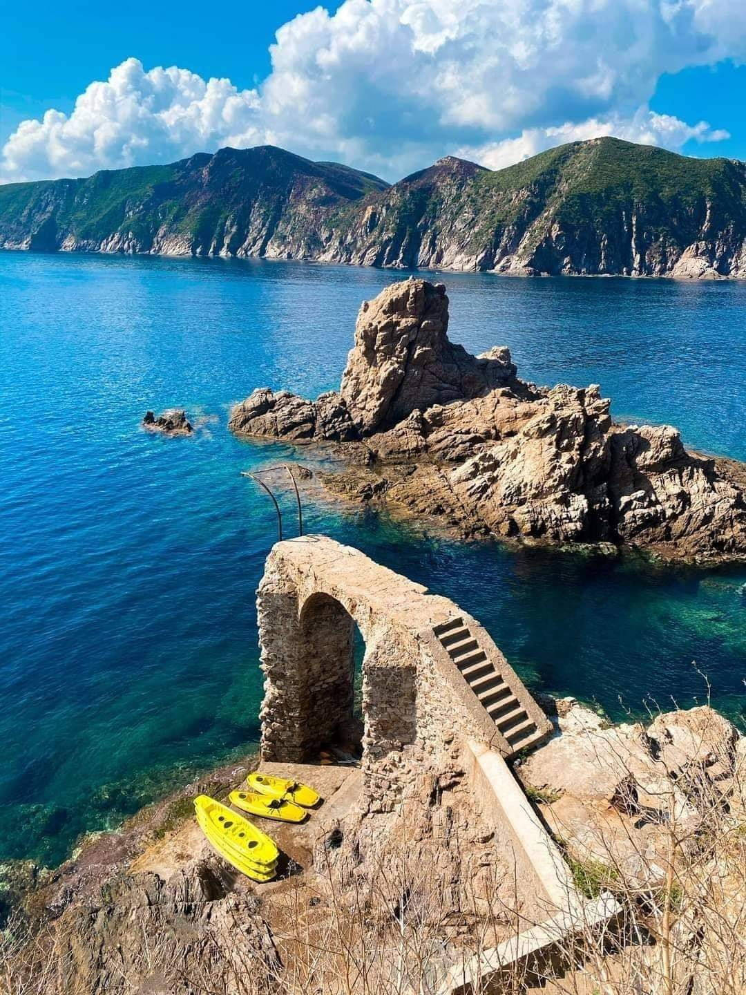 陽光普照的天空下，海邊的石頭遺跡與皮划艇 — 4K 壁紙